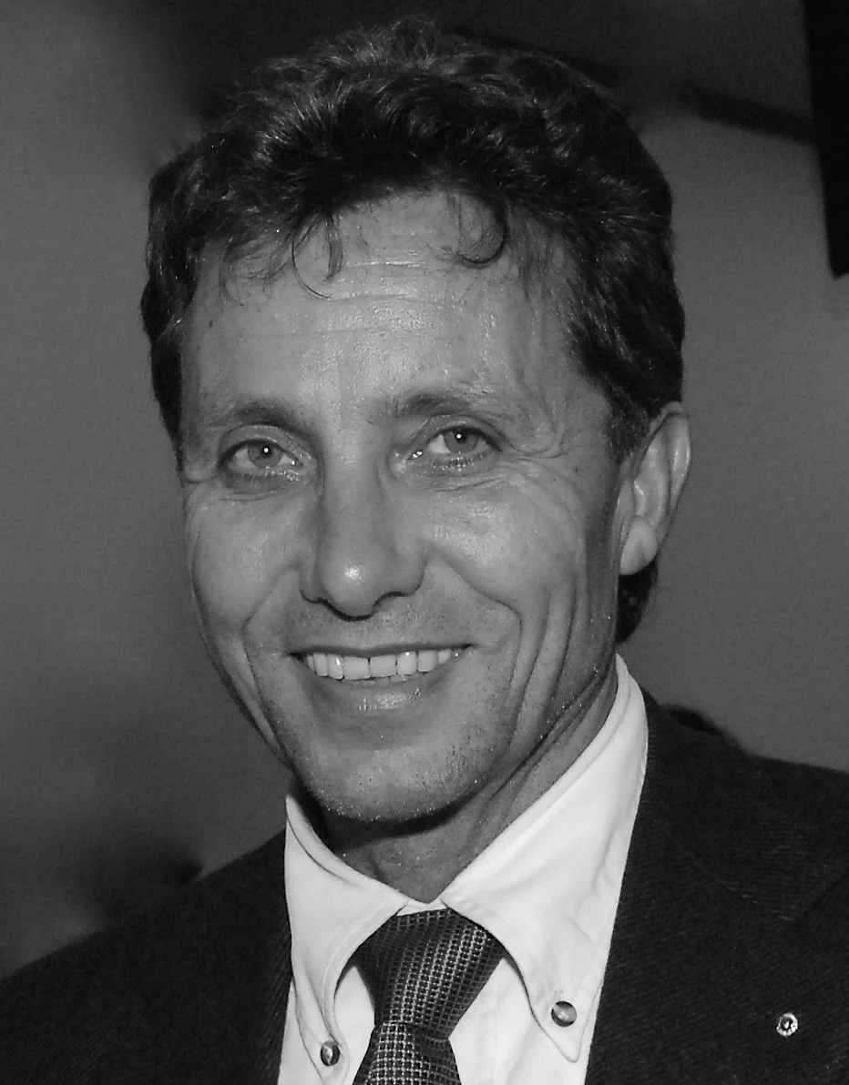 Schwarz-weiß-Foto eines lächelnden Mannes mit dunklem Haar, Anzug und Krawatte.