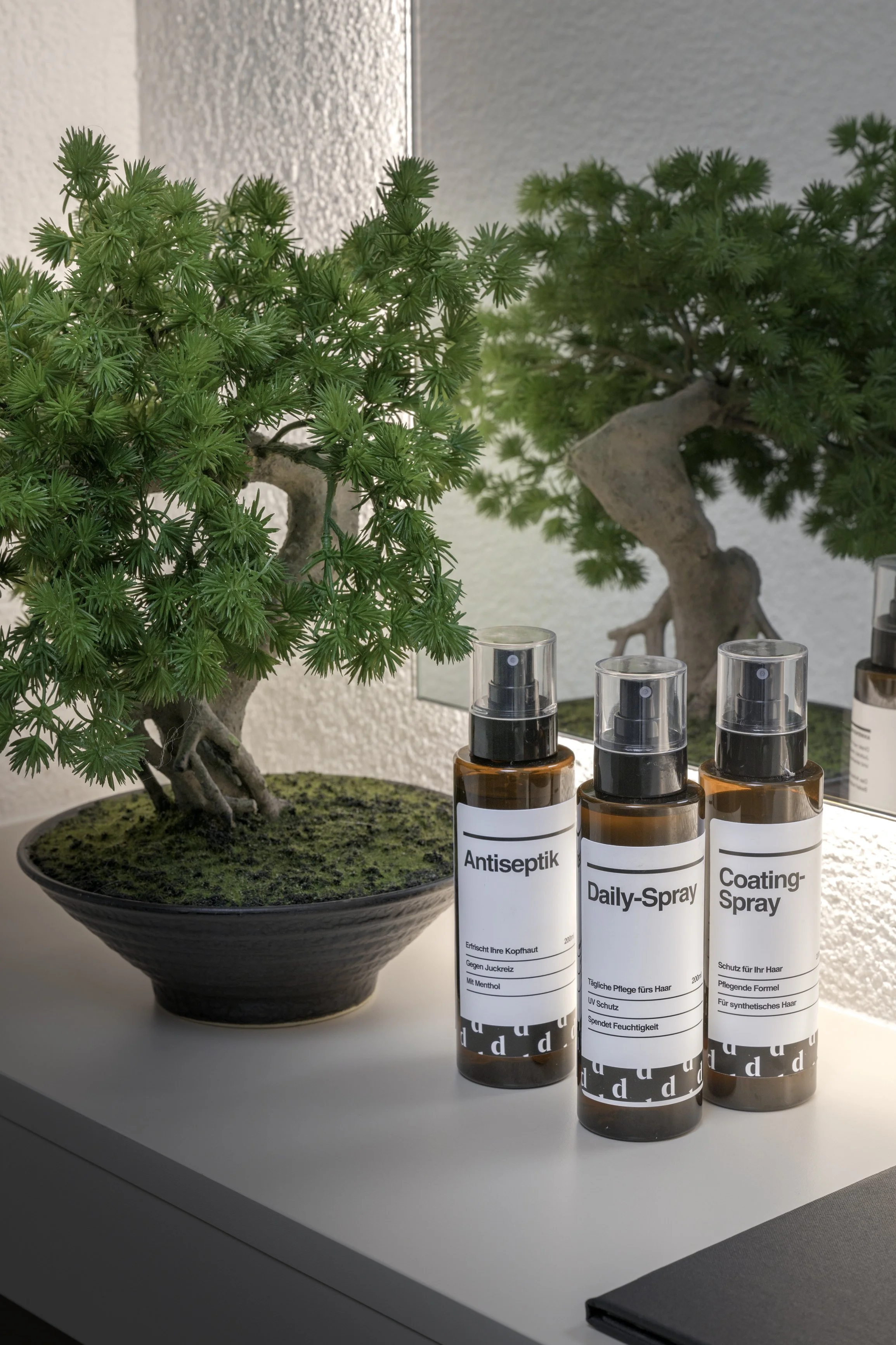 Drei Sprühflaschen auf einem Tisch neben einer Bonsai-Pflanze.