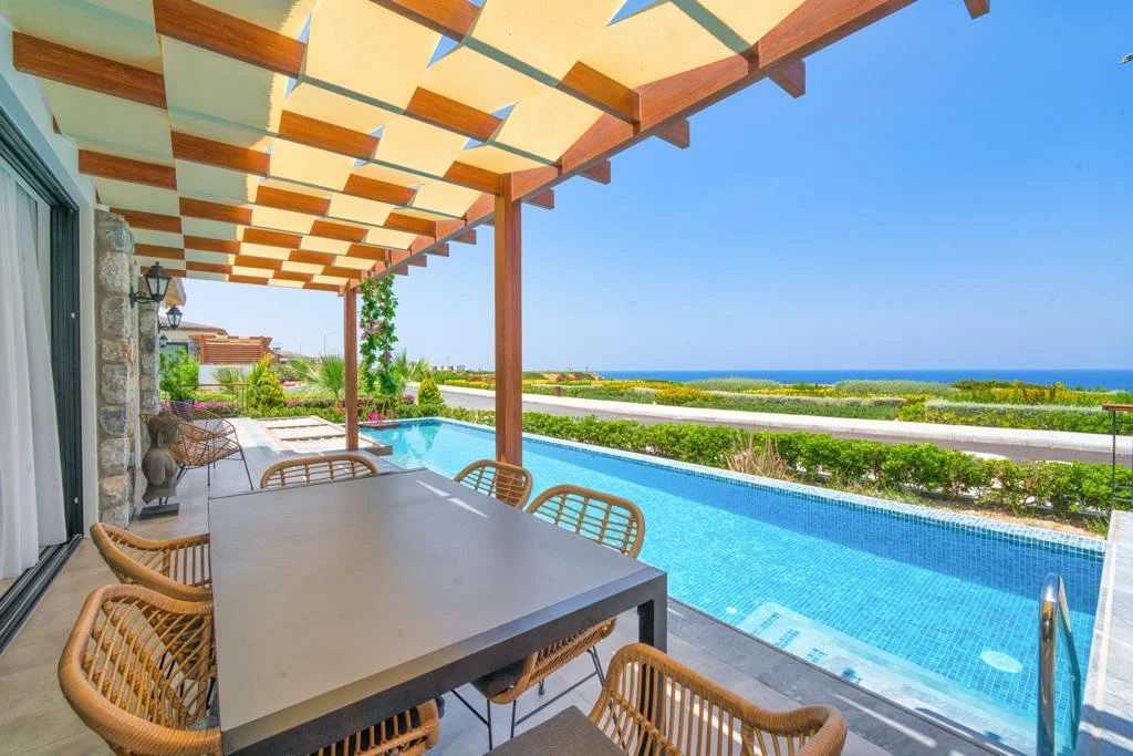 Outdoor patio area with a dining table and wicker chairs, a swimming pool, and a view of the ocean in the background.