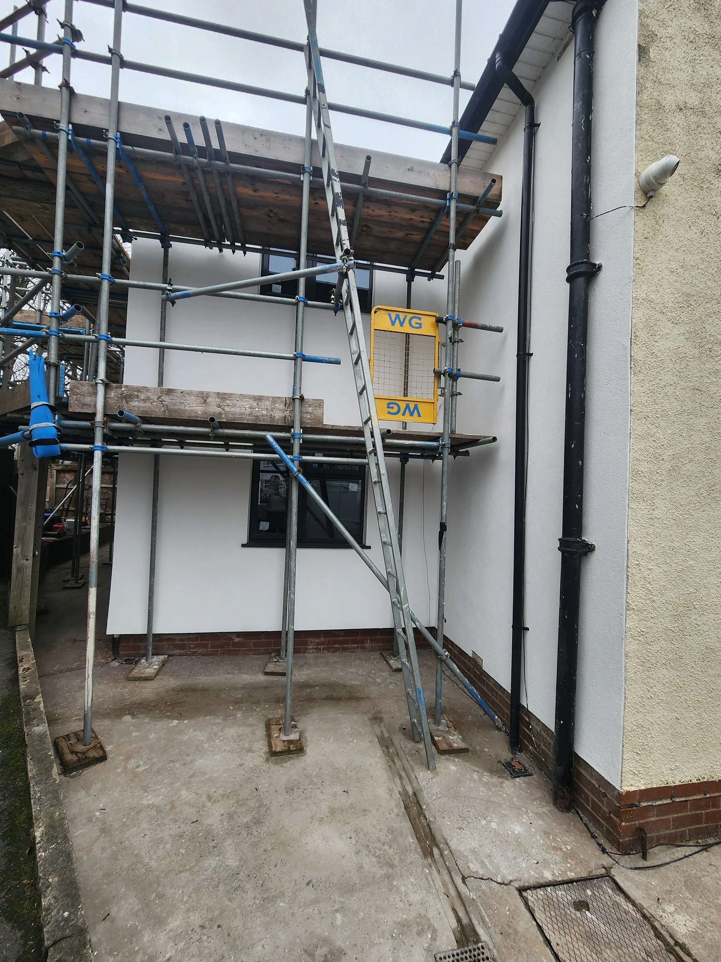 Outside of a building with construction scaffolding set up around it, and a yellow safety barrier attached to the scaffolding.