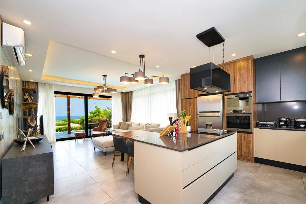 Open-concept living room and kitchen with sea view, modern decor, and large sliding glass doors.