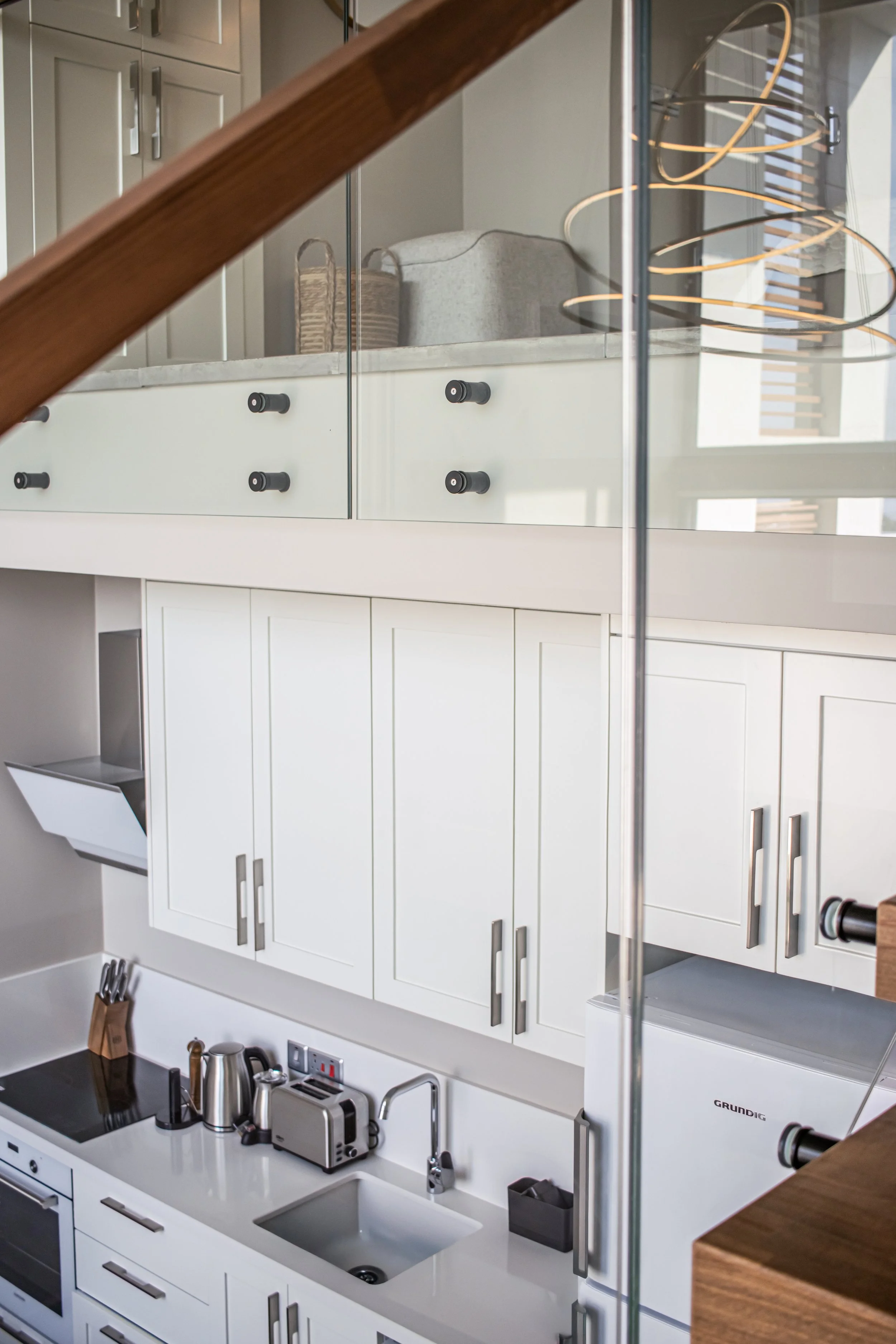 Modern kitchen with white cabinets, a small sink, a kettle, a toaster, and a three-tiered copper spiral light fixture on the ceiling.