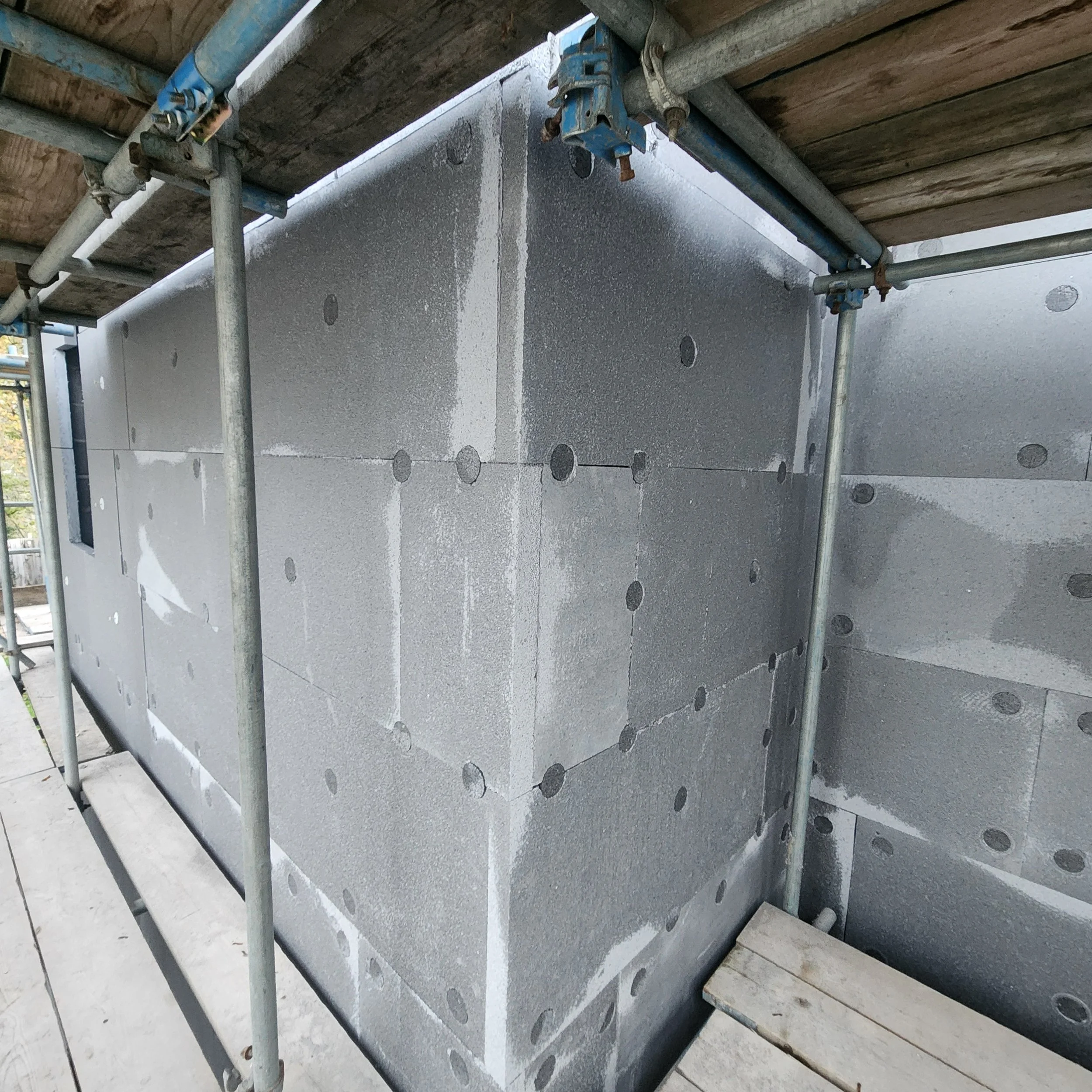 Construction site with insulated concrete panels and metal scaffolding around a building under construction.