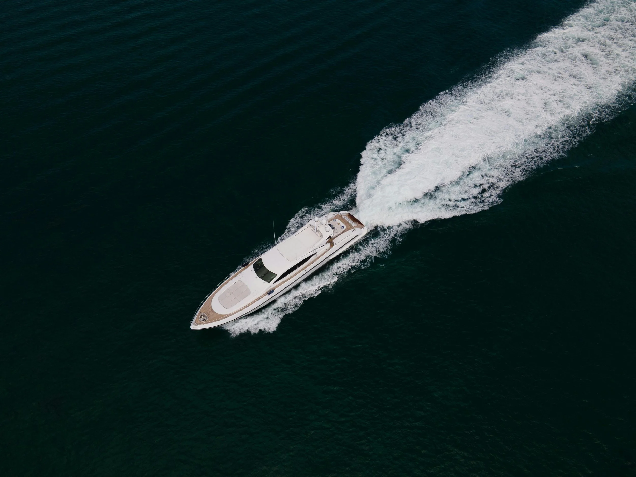 A white yacht moving at high speed across dark green waters, creating a wake behind it.