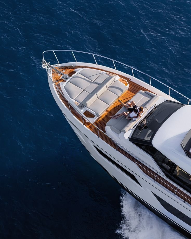 Aerial view of a luxury yacht with two people relaxing on the deck, floating on deep blue water.