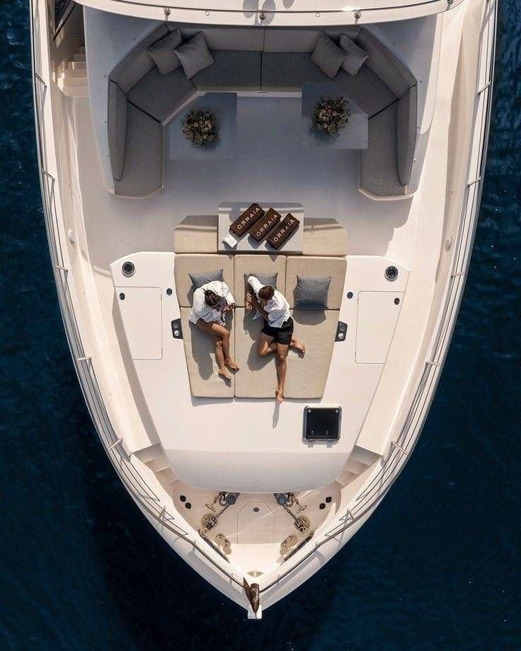 Two women relaxing on a lounge bed on the deck of a yacht, seen from above.