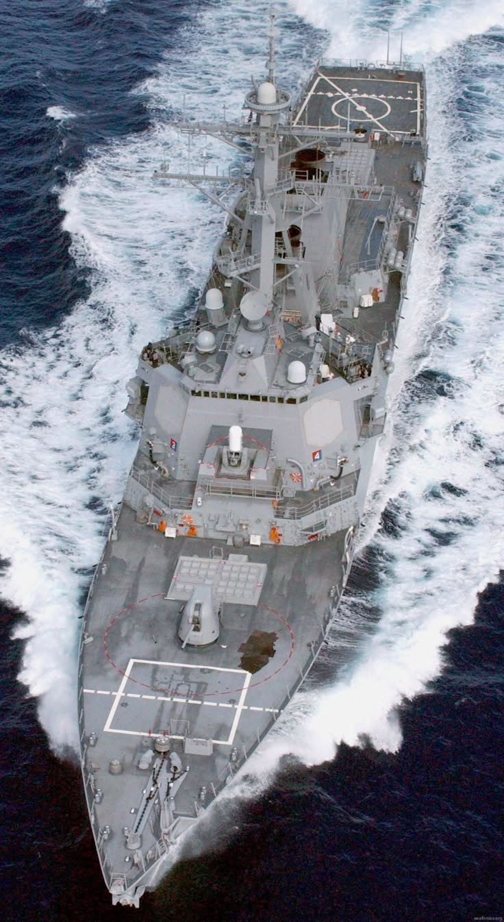 A large gray military warship sailing through the ocean, with a helipad at the back.