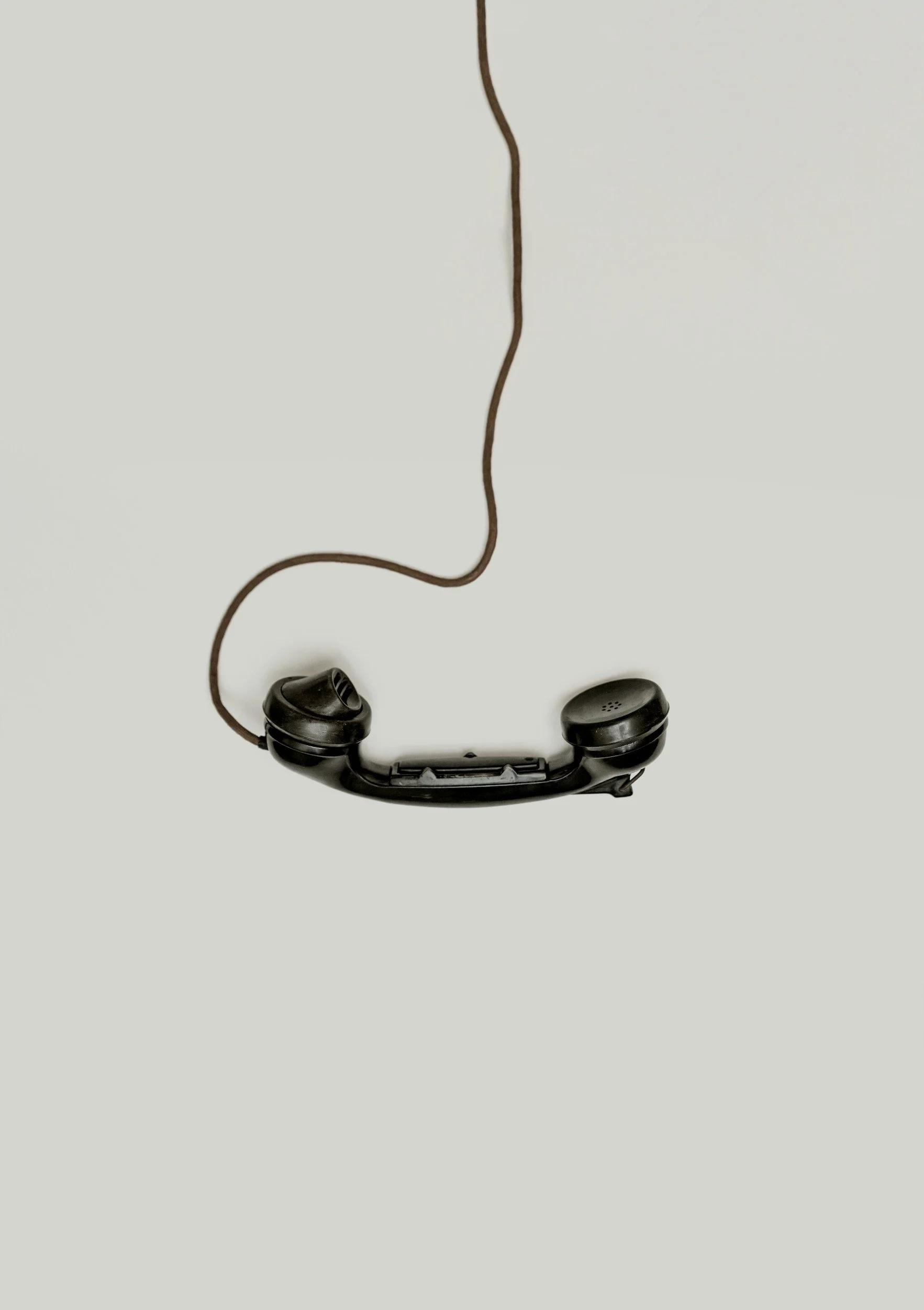 Old black telephone receiver with a wired cord, placed upside down on a plain light background.