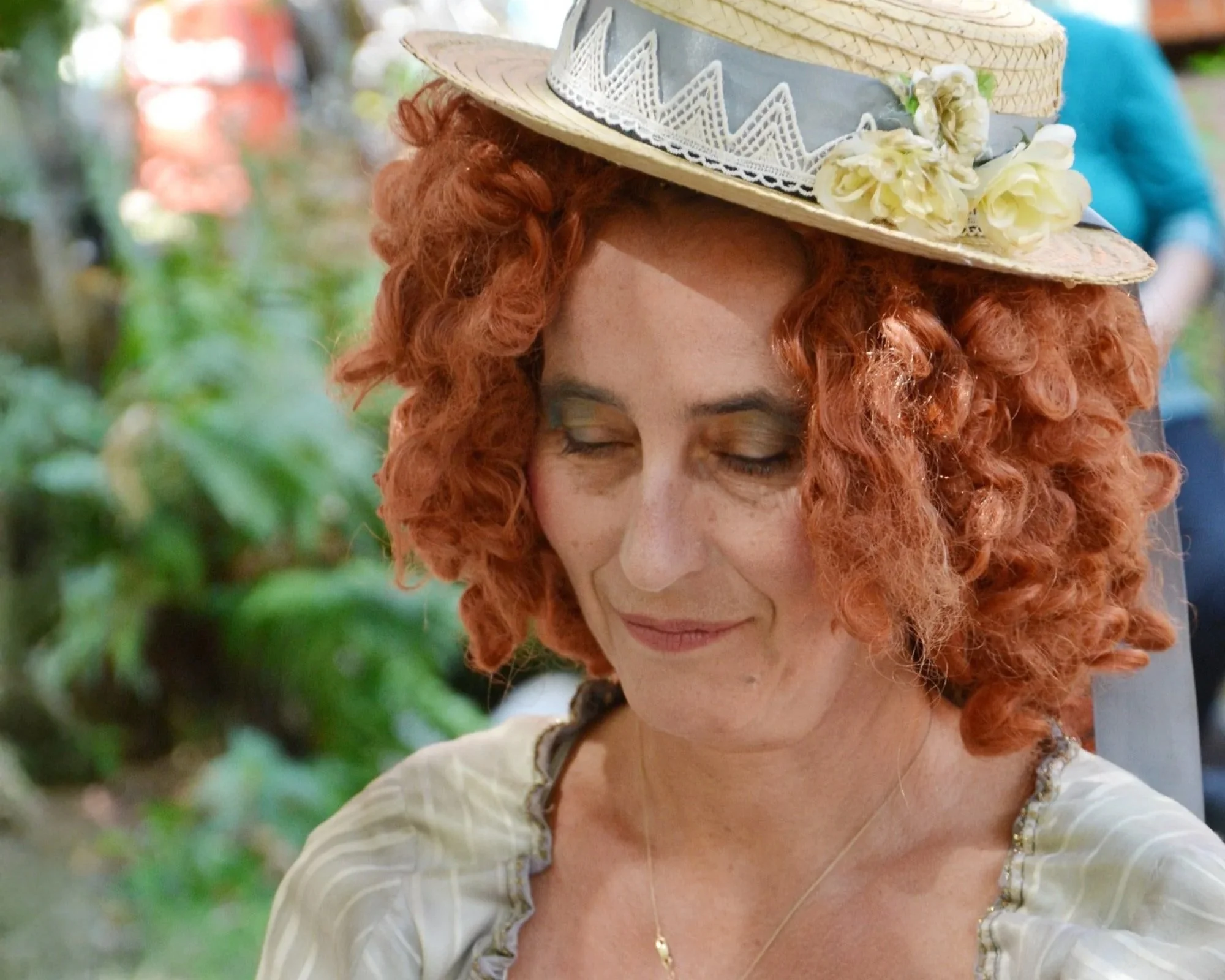 Frau mit roten Locken und Blumenhut, mit geschlossenen Augen.