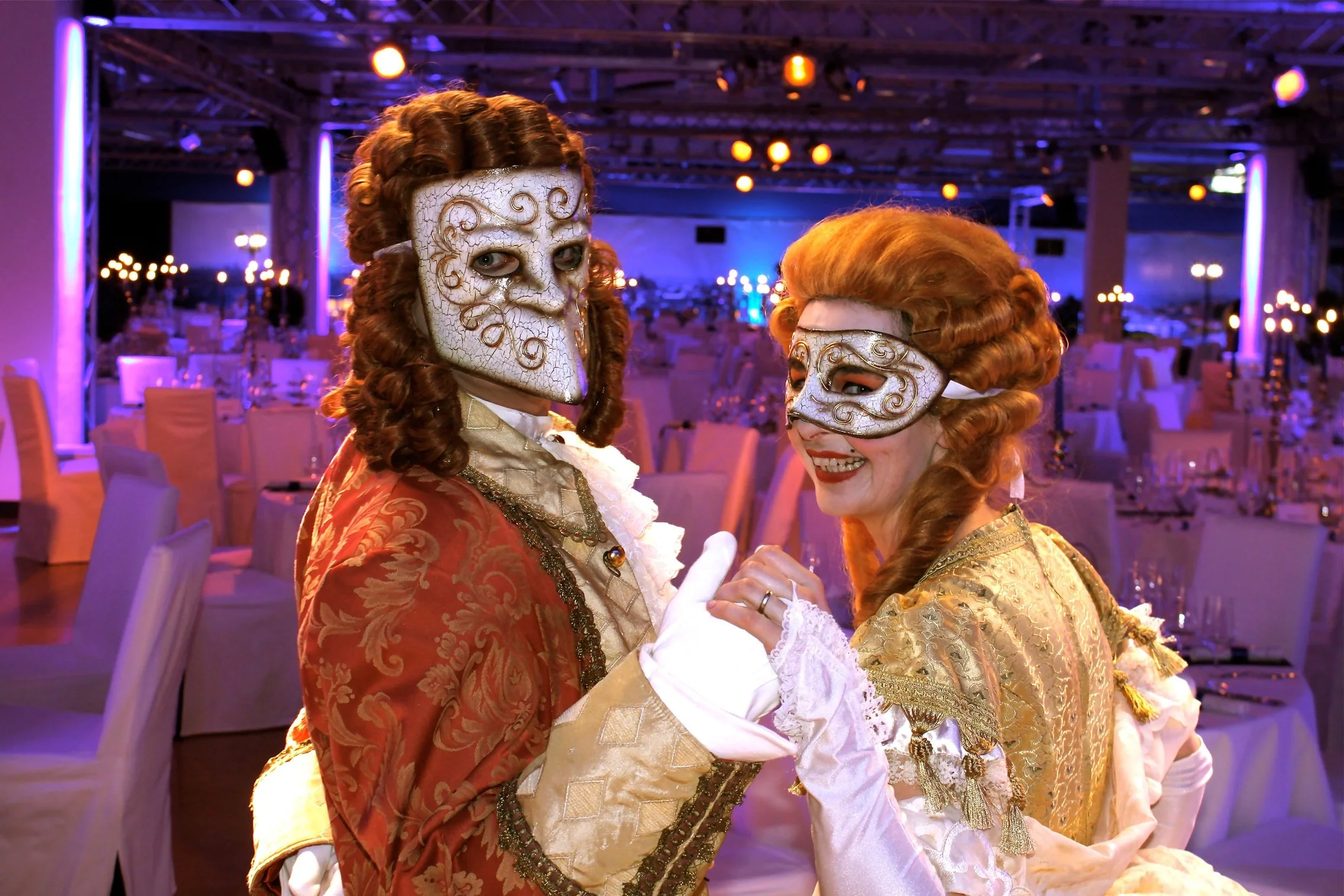 Zwei Menschen in historischen Kostümen mit Masken bei einer Maskenparty oder Kostümparty in einem festlichen Saal