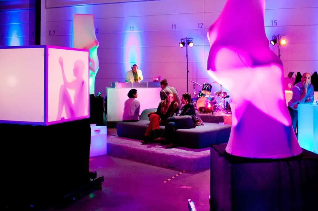 Menschen entspannen sich und feiern in einem Raum mit buntem, modernen Lichtdesign und skulpturalen Kunstwerken.