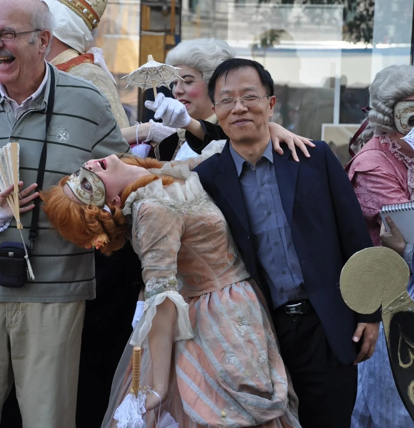 Menschen in Kostümen während einer Veranstaltung, eine Frau mit roten Haaren liegt an der Schulter eines Mannes in Anzug, andere Frauen in viktorianischen Kostümen im Hintergrund.