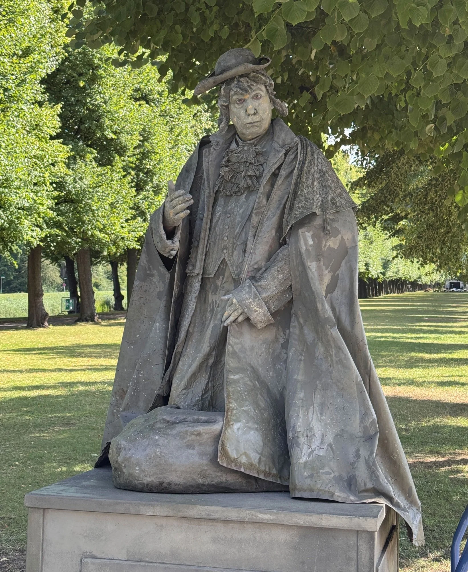 Bronzeskulptur eines Mannes in alten Kleidern mit Hut, die in einem Park steht.