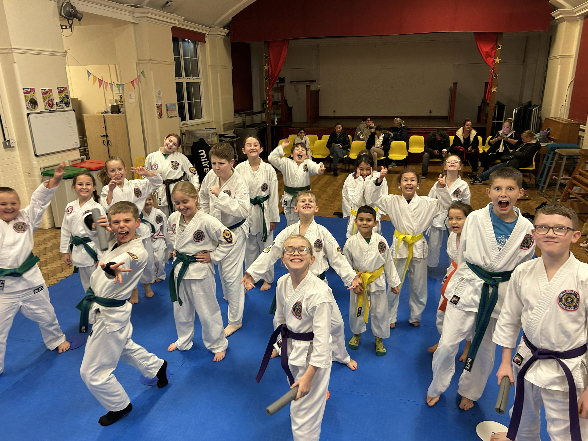 Children wearing martial arts uniforms with belts in various colors, smiling and posing for a photo in a martial arts studio.