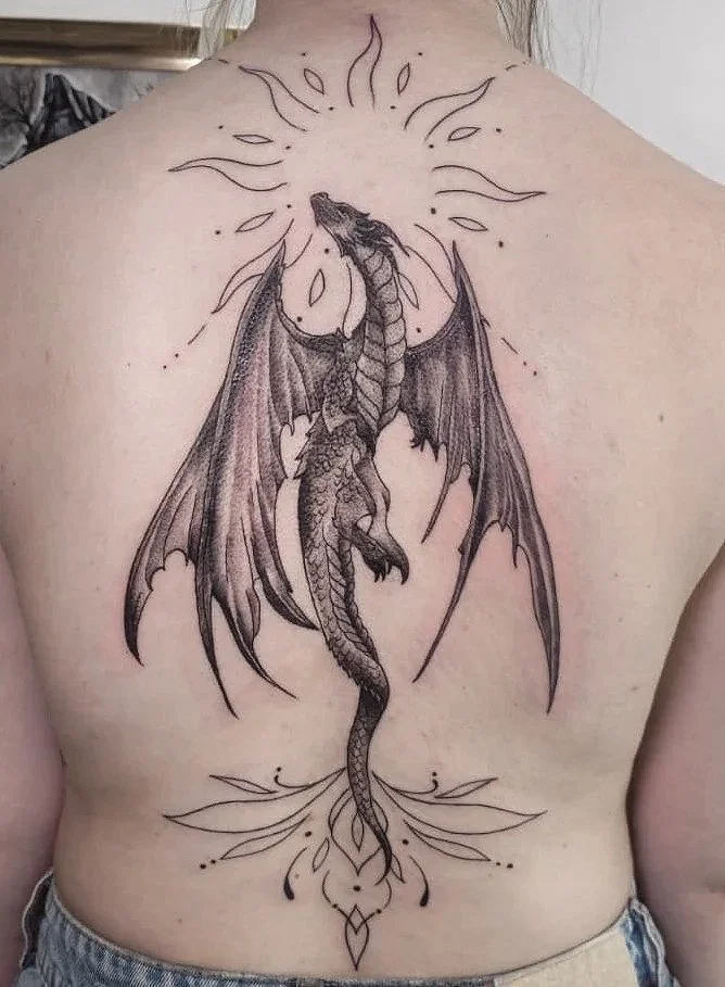 Tatuaje de un dragón en el centro de la espalda que parece elevarse, rodeado de líneas decorativas y efectos de luz.