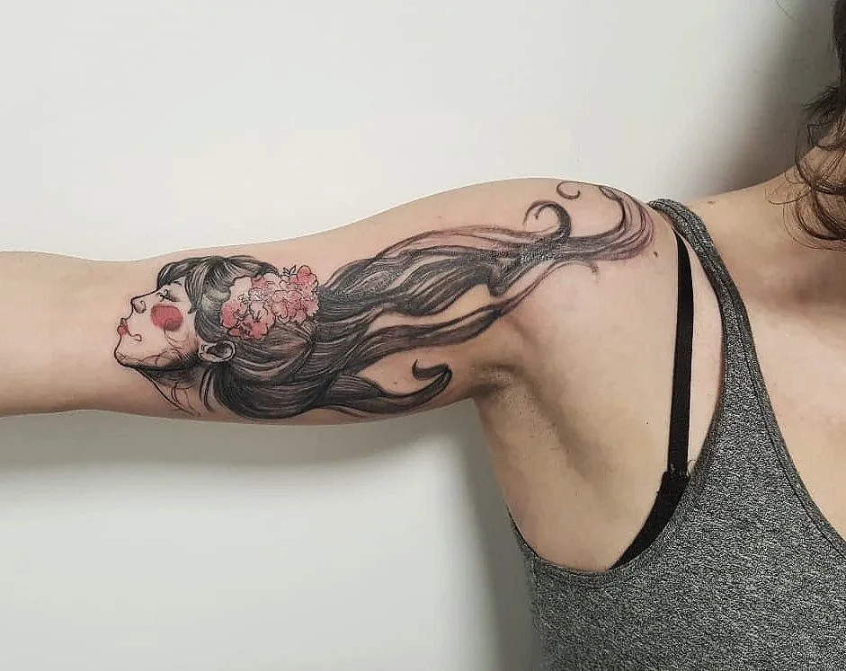 Tatuaje de una mujer con cabello largo y flores rosadas en el cabello en el brazo de una persona.