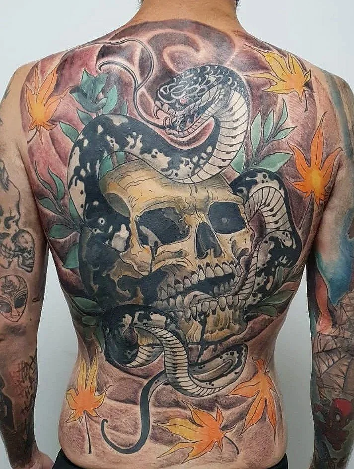 Tatuaje de una calavera rodeada de serpientes y hojas de arce en el abdomen y pecho.