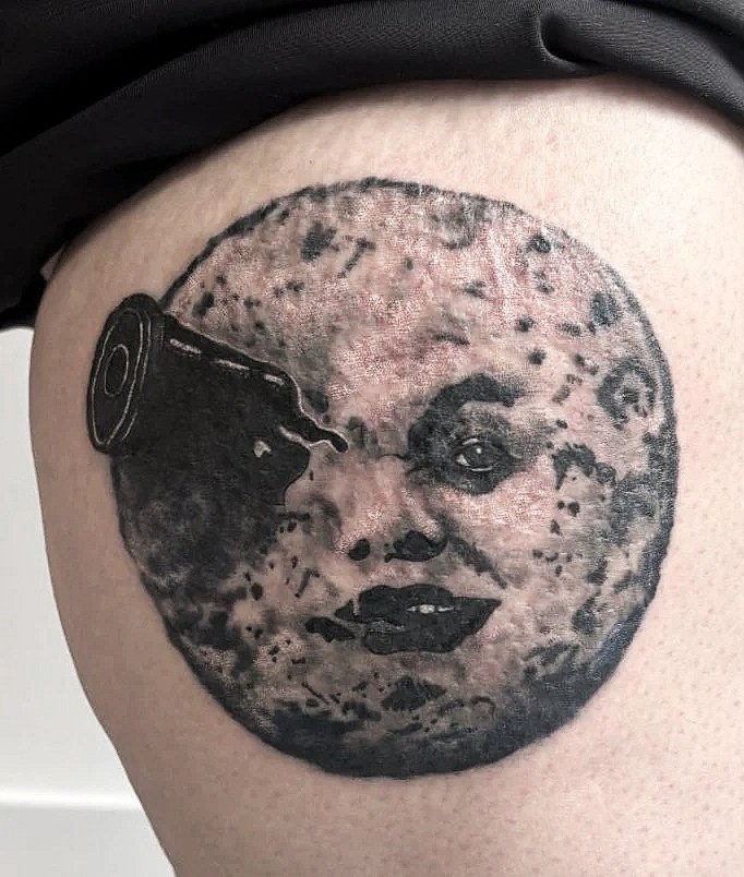 Tatuaje de la luna con cara en la piel, con una lata que vierte líquido sobre su frente.