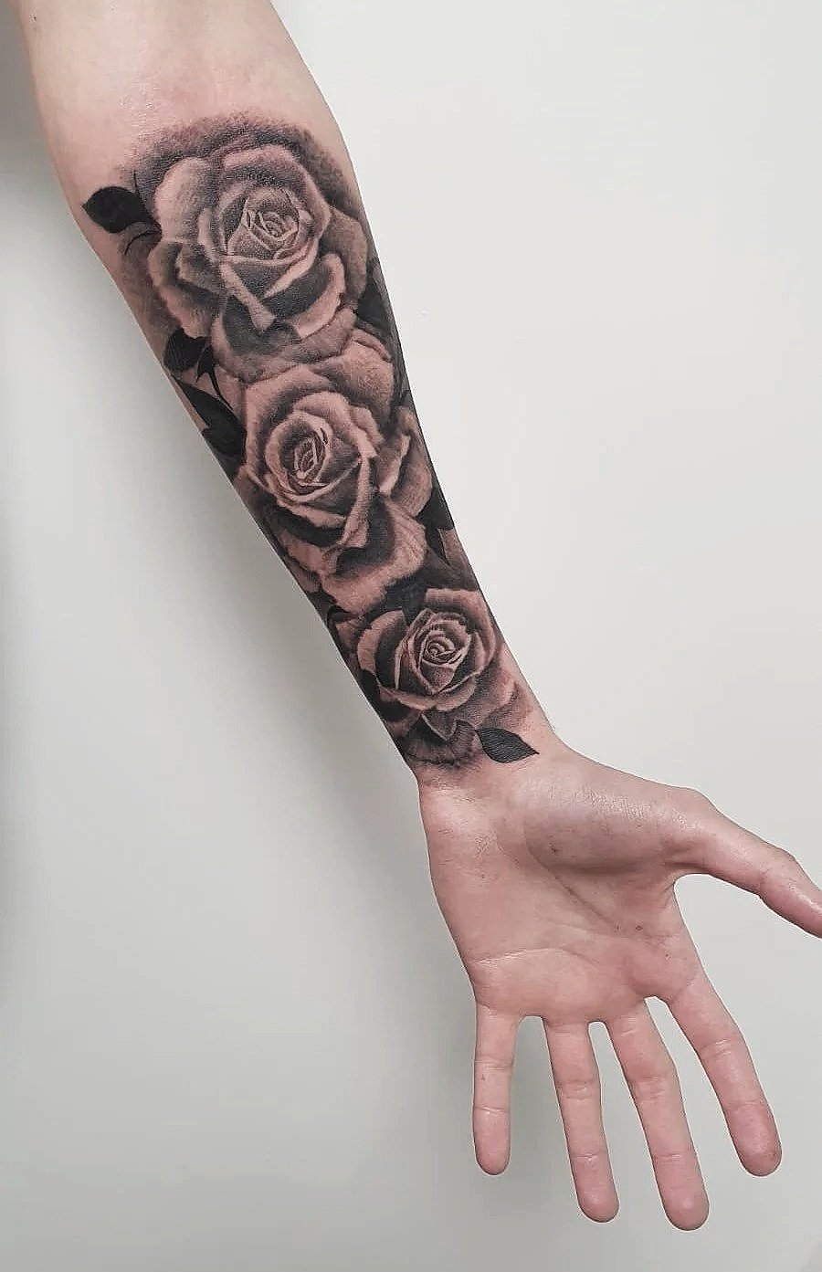 Tatuaje en el antebrazo de varias rosas en tonos negros y grises con hojas oscuras.