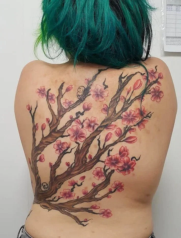 Tatuaje de un árbol de cerezo en la espalda de una persona con cabello verde.