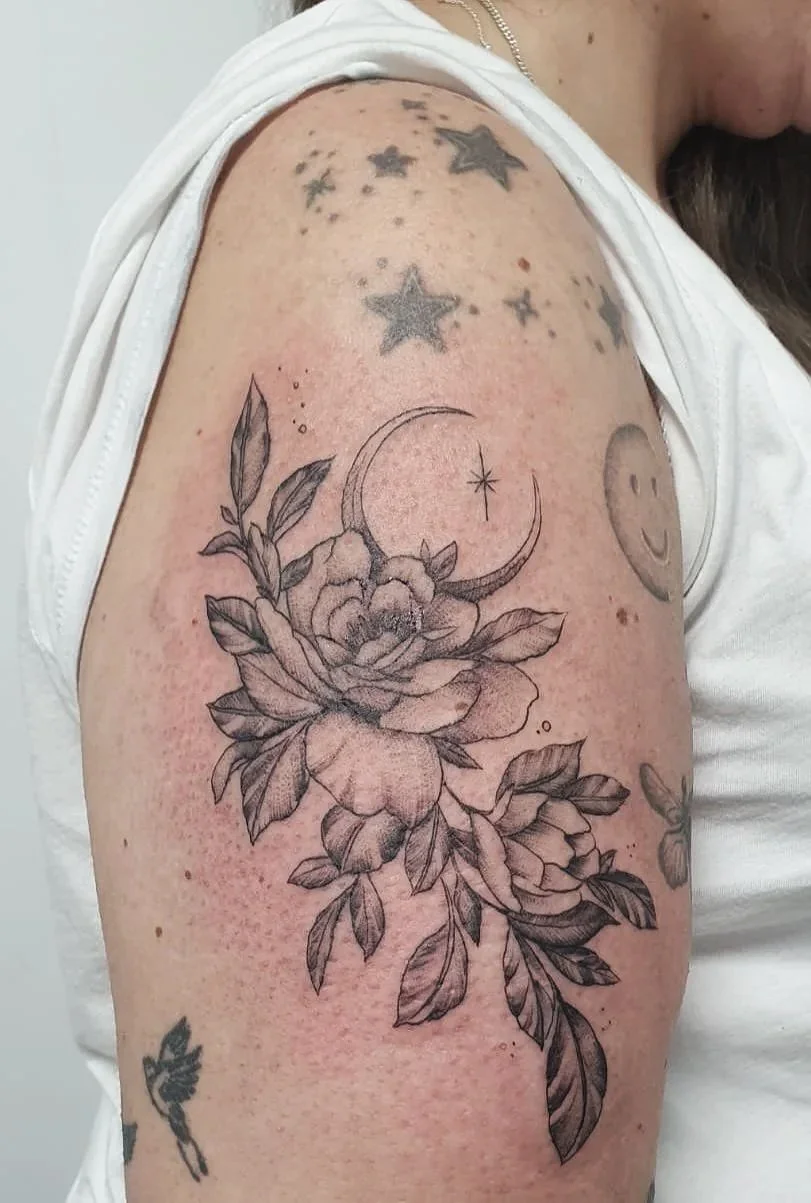 Tatuaje de una rosa con hojas y una luna con estrella en la parte superior, en el brazo de una persona.