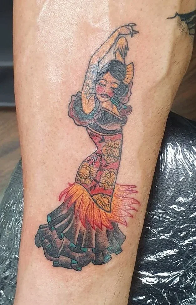 Tatuaje de una mujer bailando, con un vestido colorido y flores, en estilo cartoon, en la parte superior del muslo.