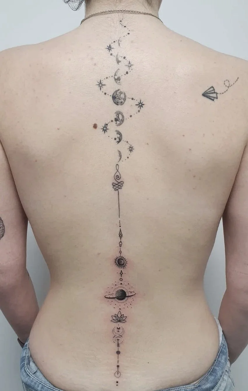 Tatuaje en la espalda que representa un diseño de elementos cósmicos y astronómicos, incluyendo planetas, estrellas, la luna y el sol.