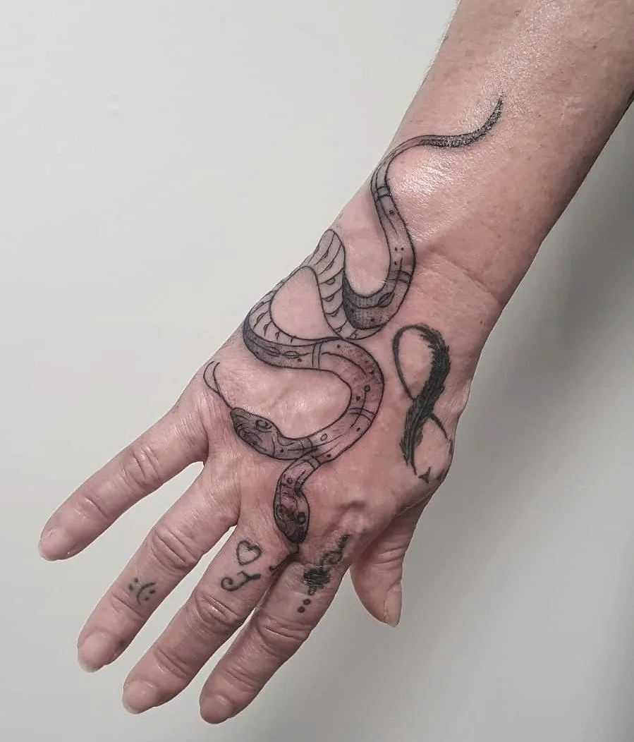 Tatuaje de una serpiente en el dorso de la mano, con detalles en negro y algunos espacios en blanco.