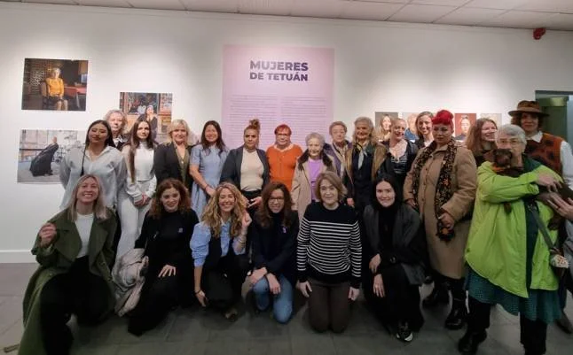 Grupo de personas posando frente a un cartel que dice 'Mujeres de Tetuán', en una galería con fotos en las paredes.