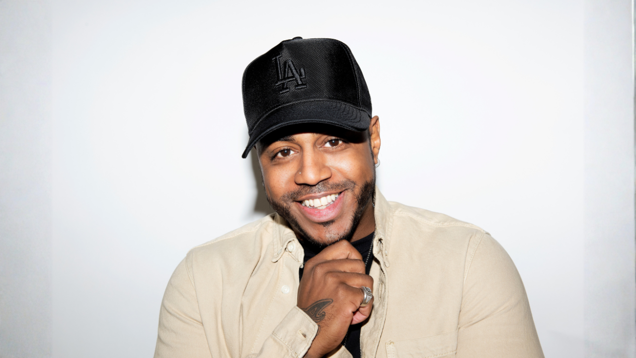 Bradley from S Club  wearing a black baseball cap and beige shirt, posing against a plain white background.