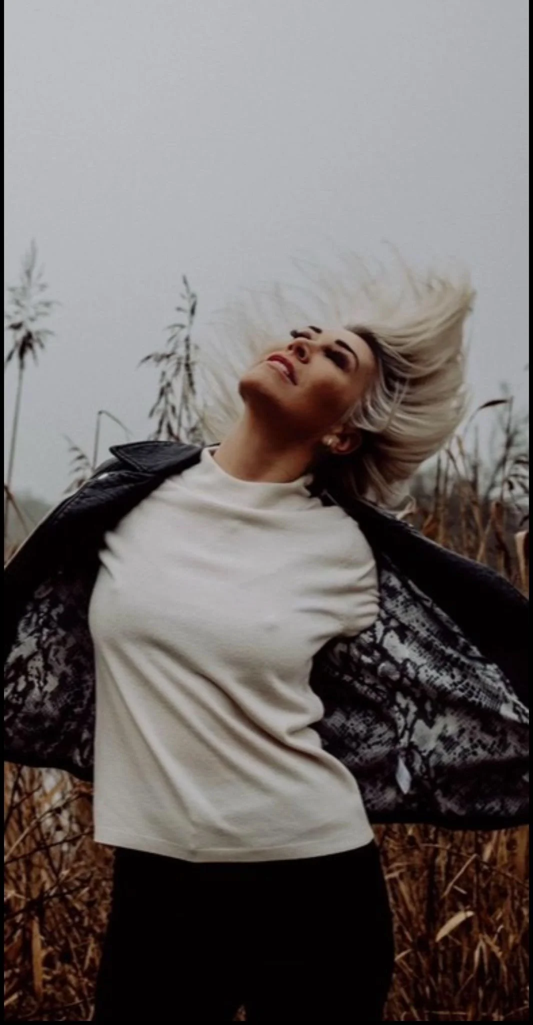 Jo O'Meara from S Club with platinum blonde hair leaning back in a field of tall dry grass on an overcast day.