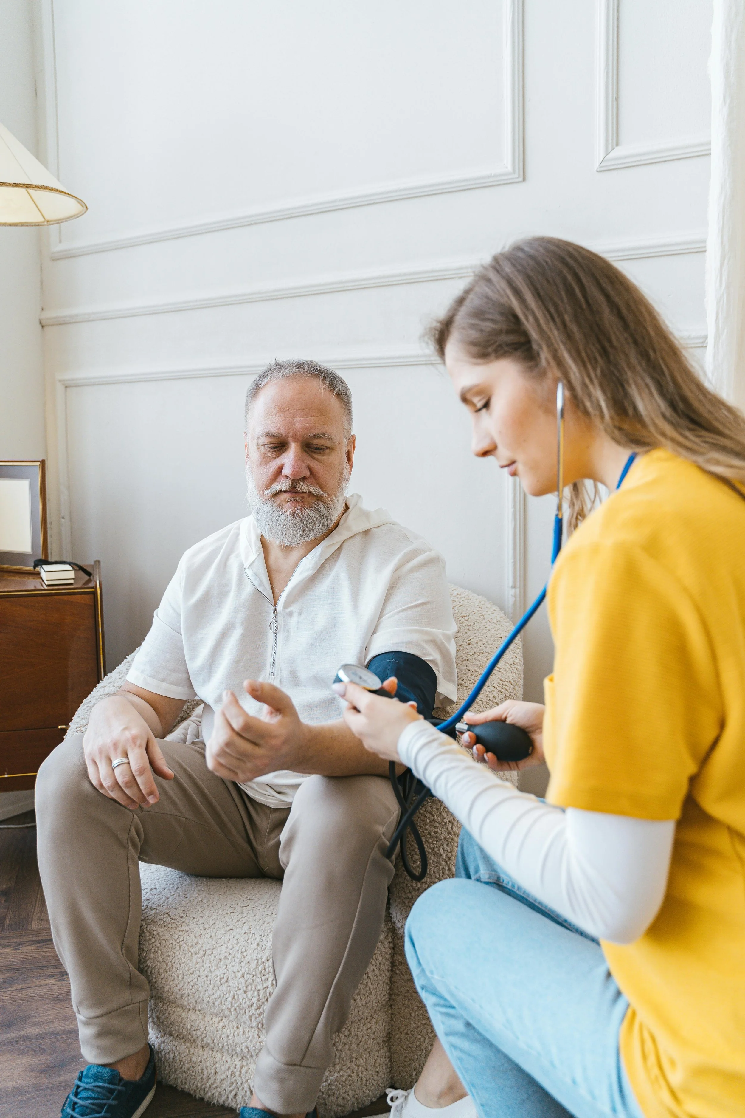 A young female healthcare worker taking the blood pressure of an older man in a living room.