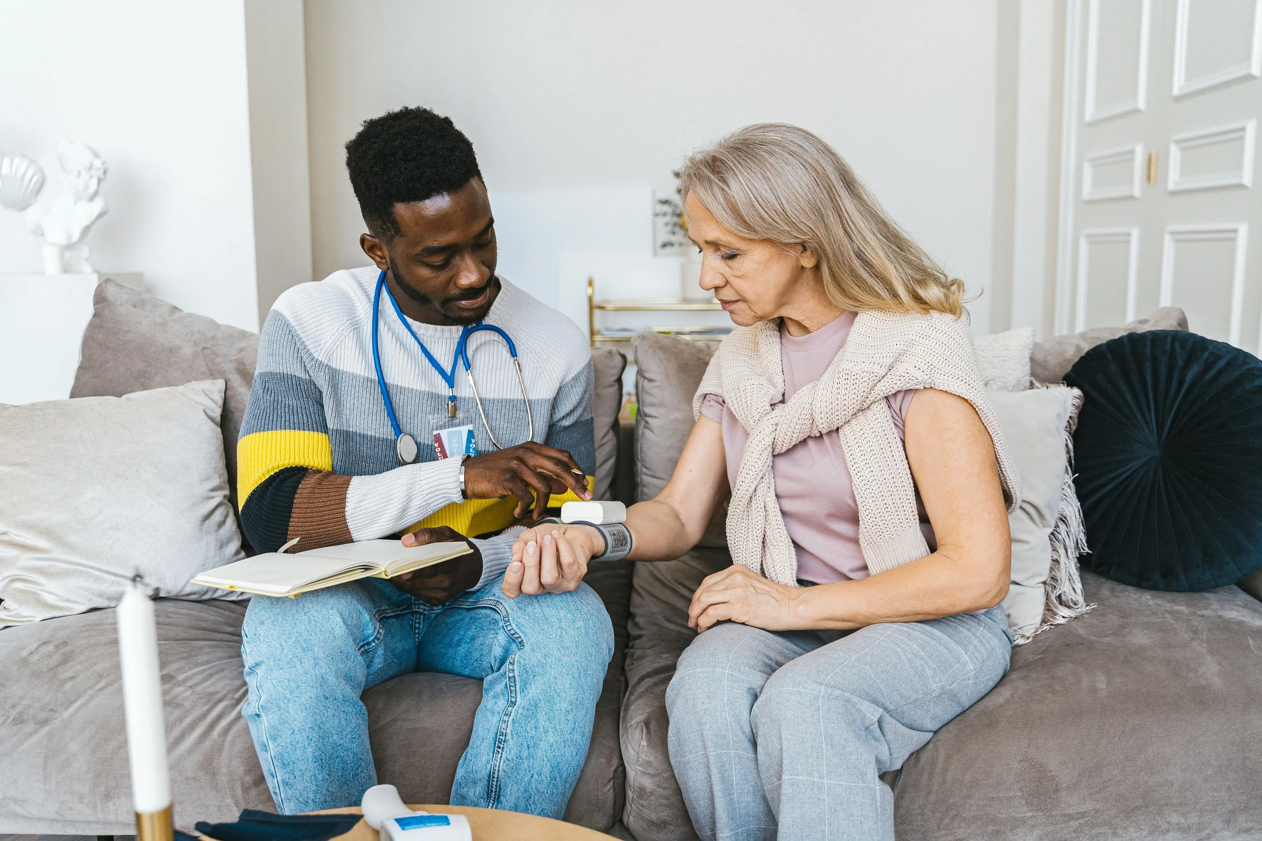 A healthcare professional checks an elderly woman's blood pressure at home.