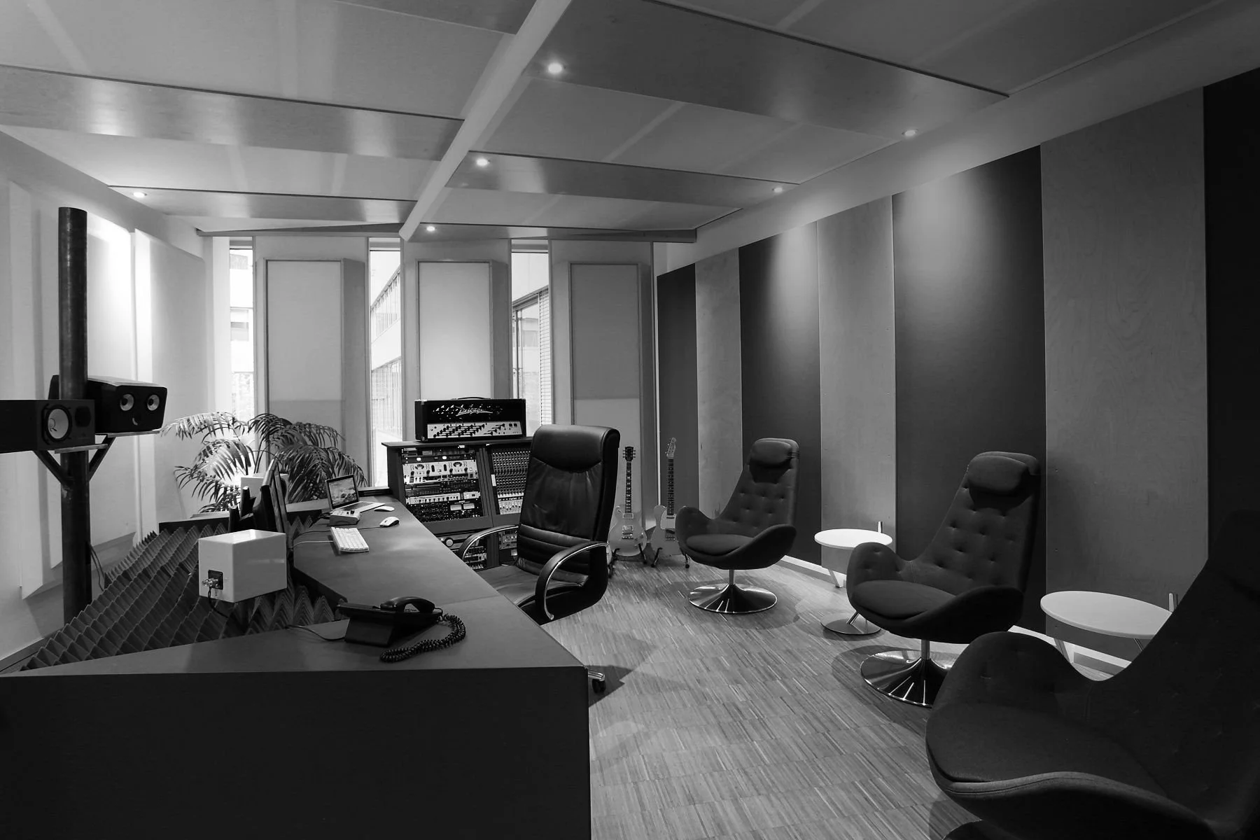 Aufnahme eines Tonstudios mit Schreibtisch, mehreren Stühlen, Musikinstrumenten und moderner Akustik-Deckenschallisolierung.