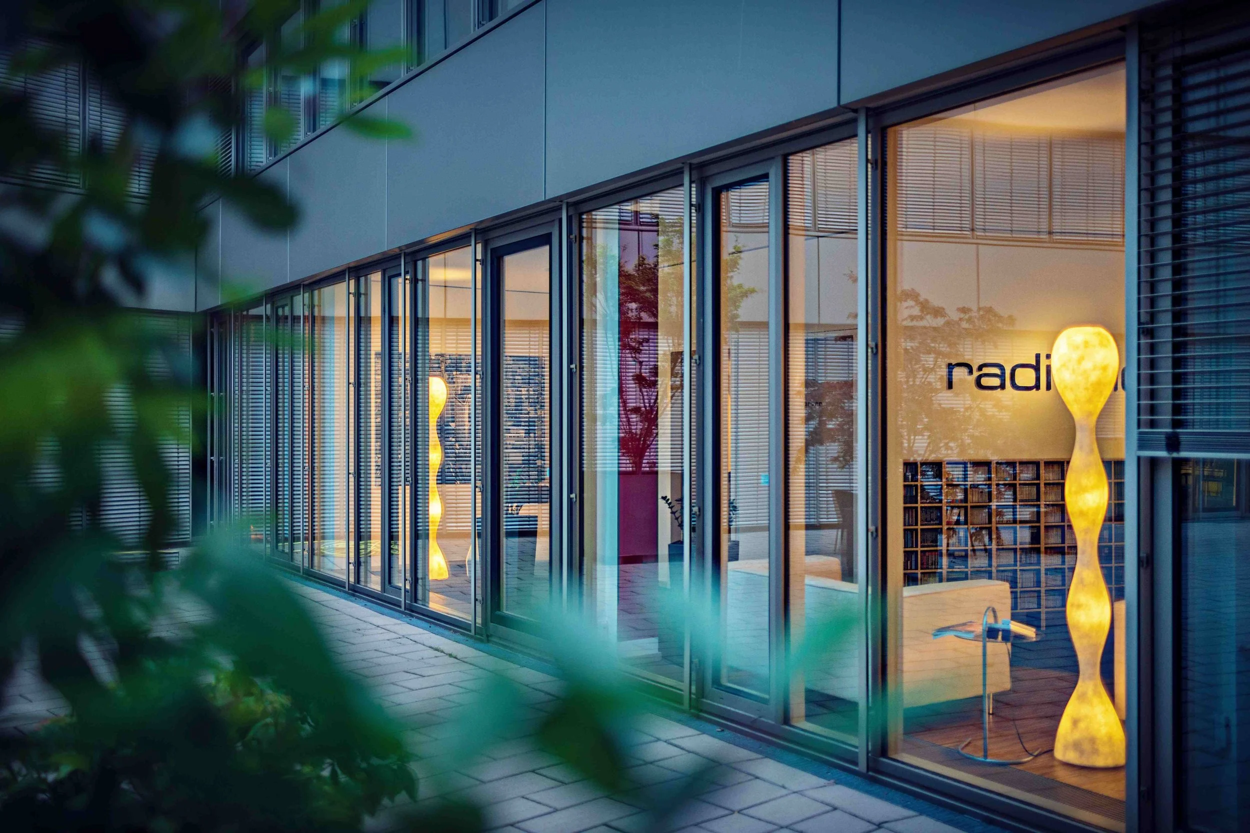 Moderne Bürogebäude mit Glasfenstern und dekorativen Lampen im Inneren, Blick durch die Fenster bei Dämmerung.