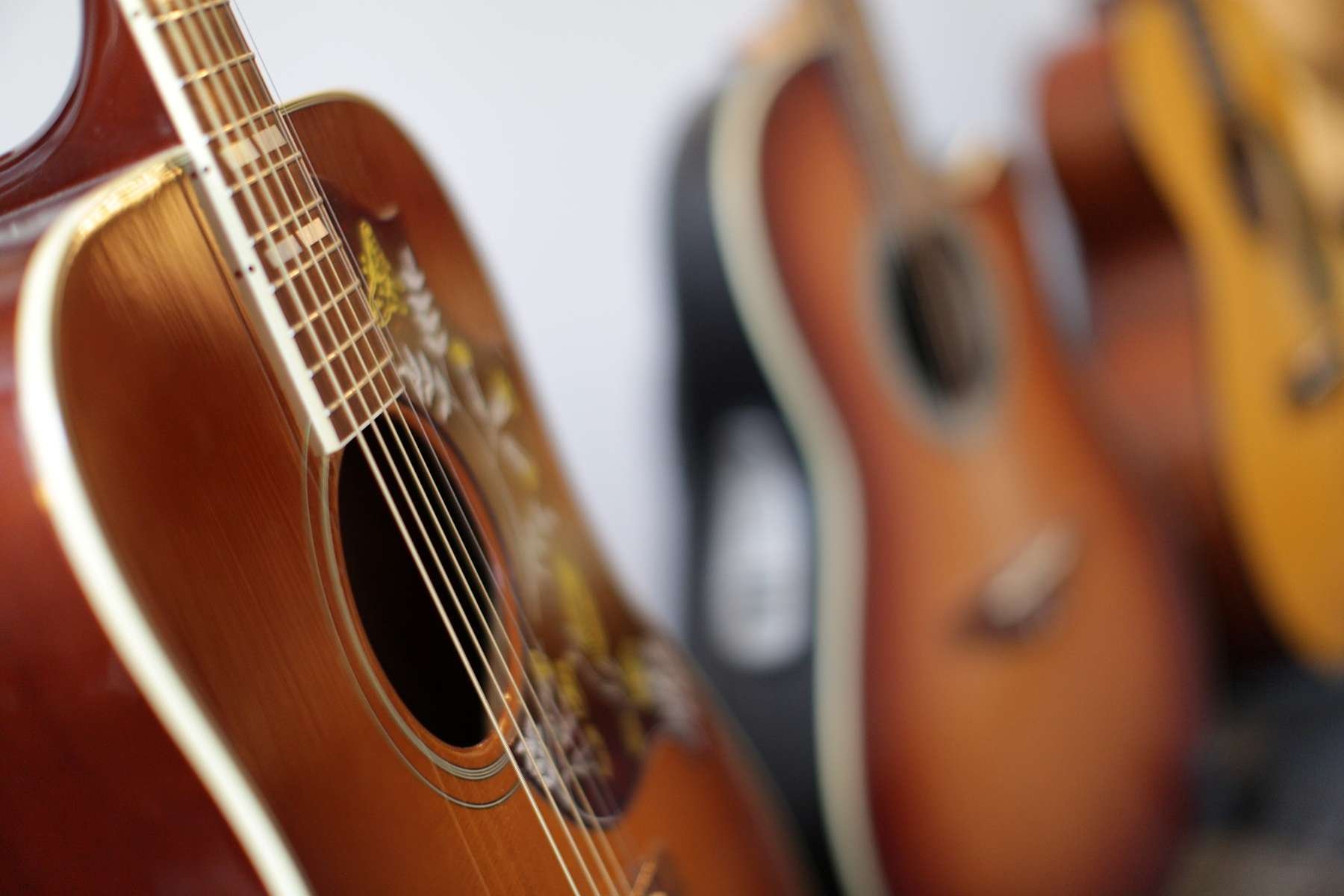 Mehrere akustische Gitarren hängen an der Wand, im Fokus eine braune Gitarre im Vordergrund, unscharfe weitere Gitarren im Hintergrund.