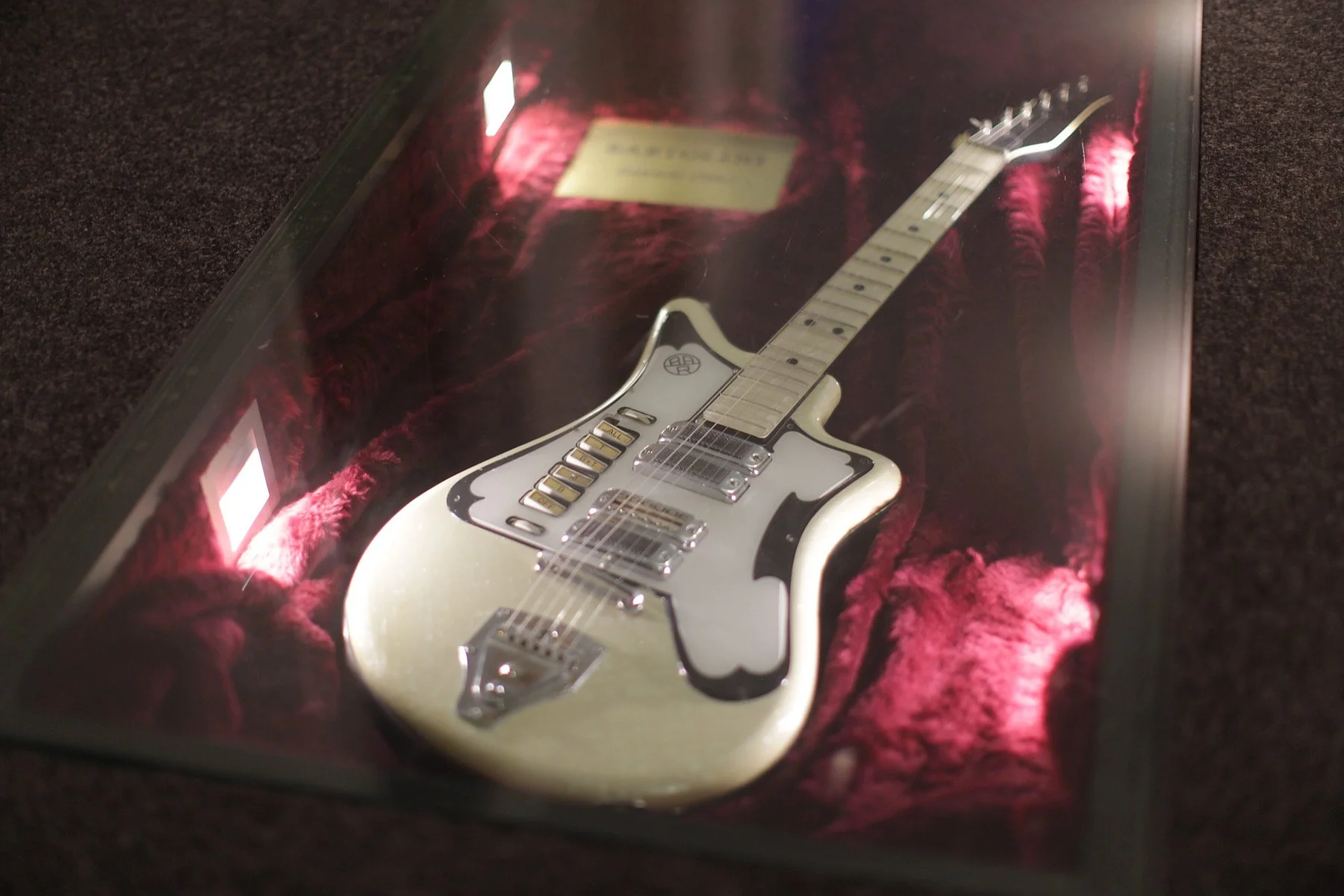 Ein silberfarbenes elektrisches Gitarre in einem gläsernen Ausstellungsdisplay mit rotem Samt im Inneren.