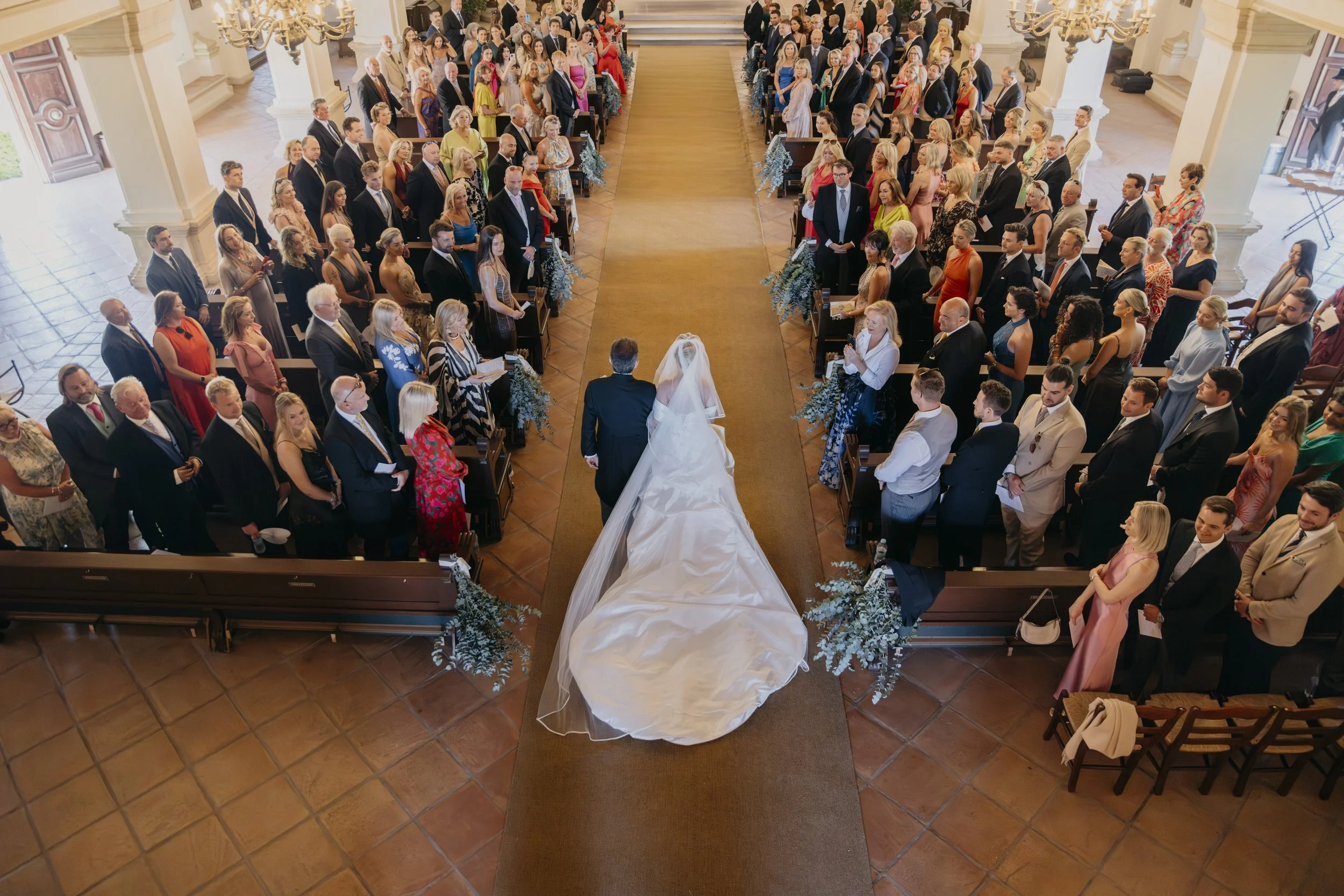 A wedding ceremony taking place in a church, with a bride and groom walking down the aisle as guests look on.