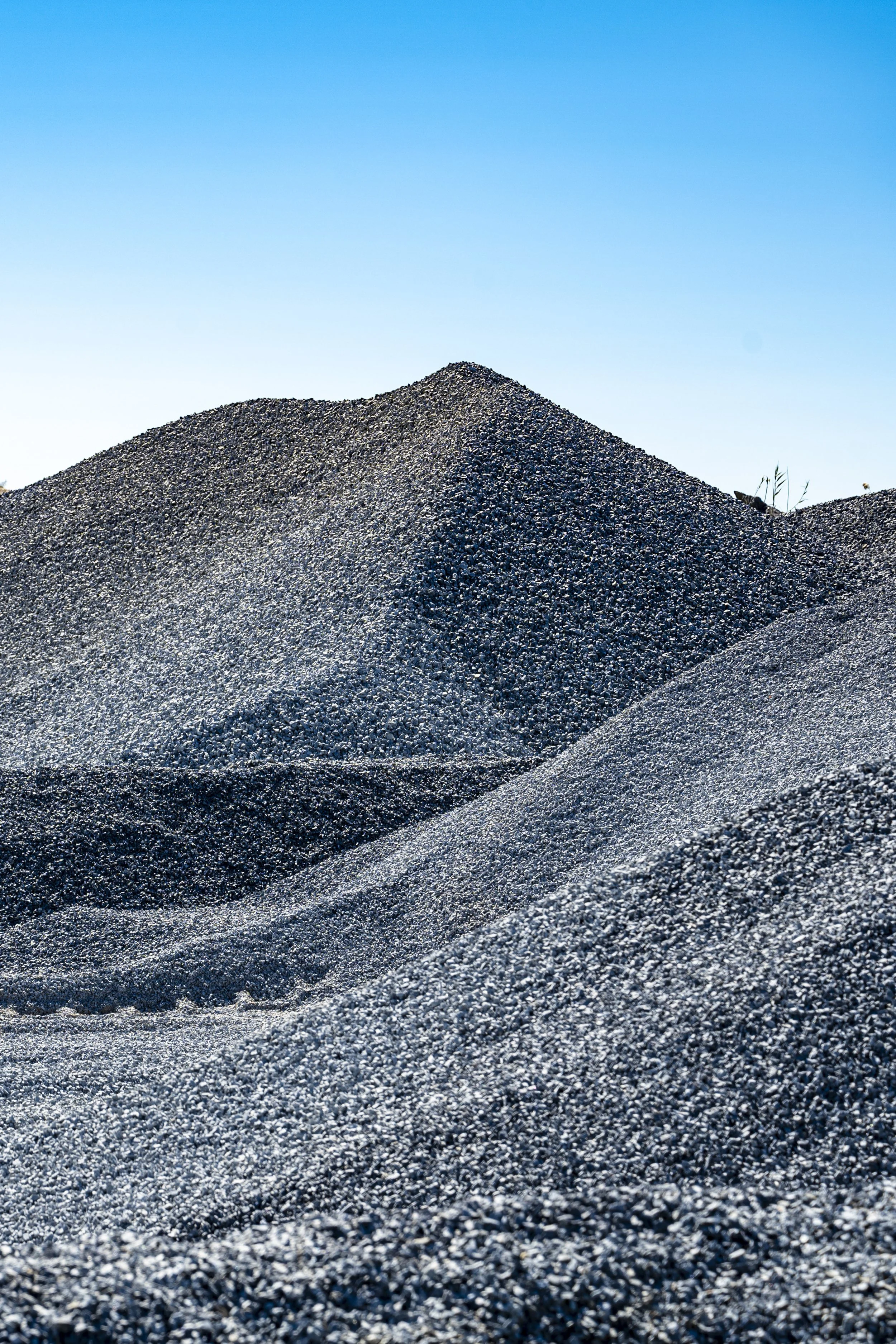 Close-up view of several large piles of black gravel or crushed stones against a clear blue sky.