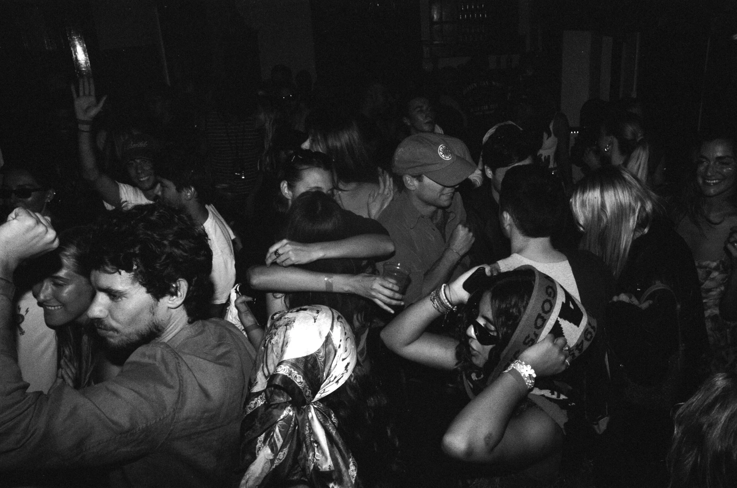 A black and white photograph of a lively party with women and men dancing and celebrating closely together.