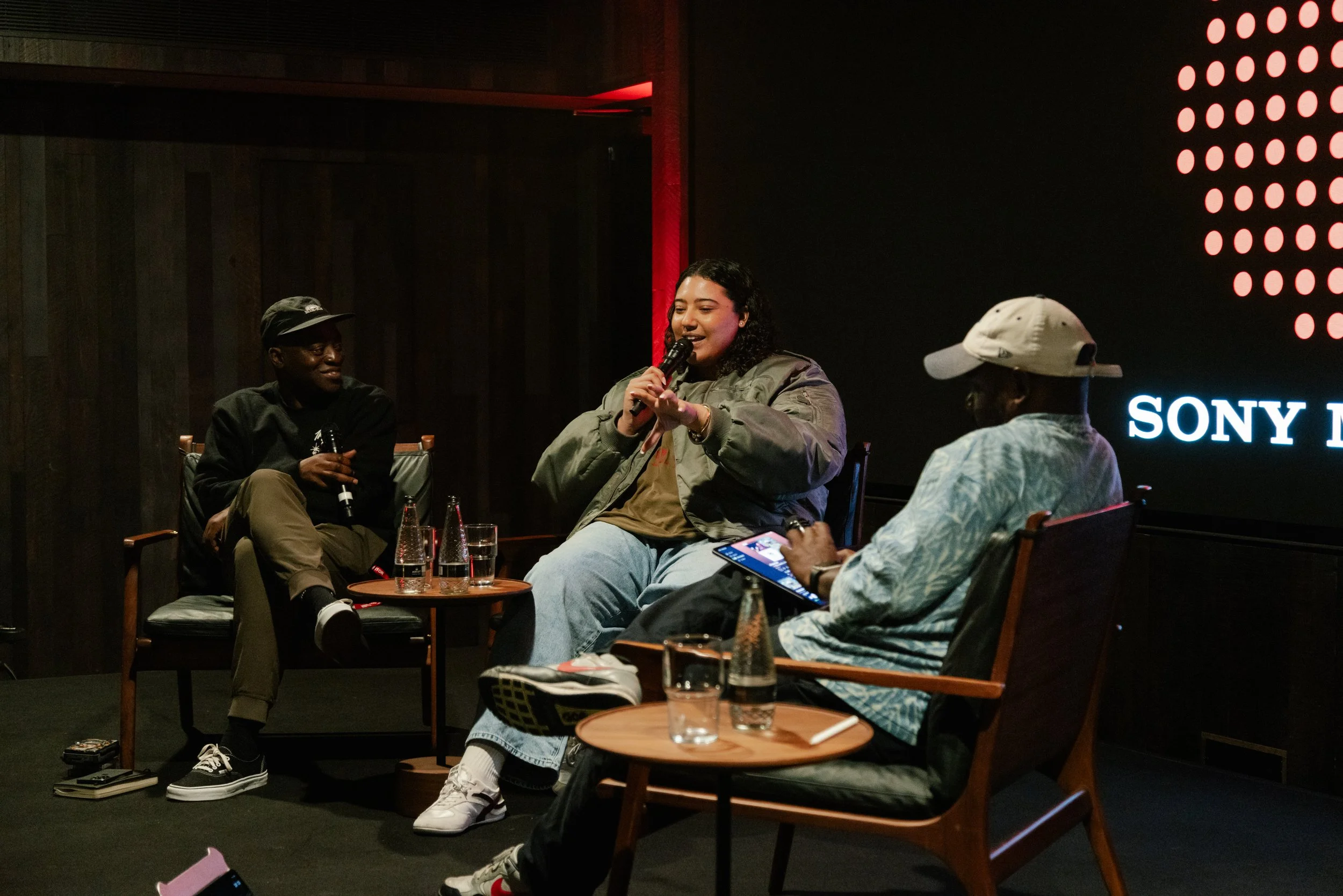 A panel discussion with three people seated on stage, one woman speaking into a microphone, with a dark background and the Sony logo visible.