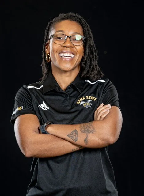 Coach P (Camise Patterson) smiling at the camera while her arms are folded.