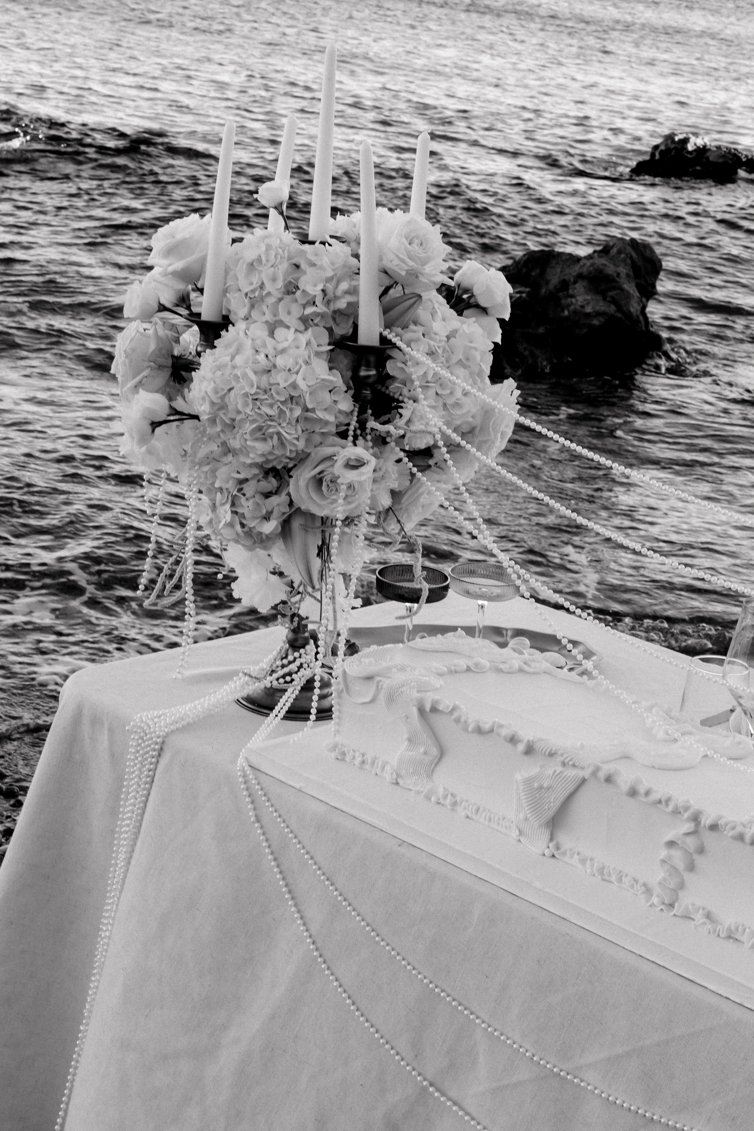 Table de mariage décorée avec une composition florale, des bougies et des perles, située près de la mer.