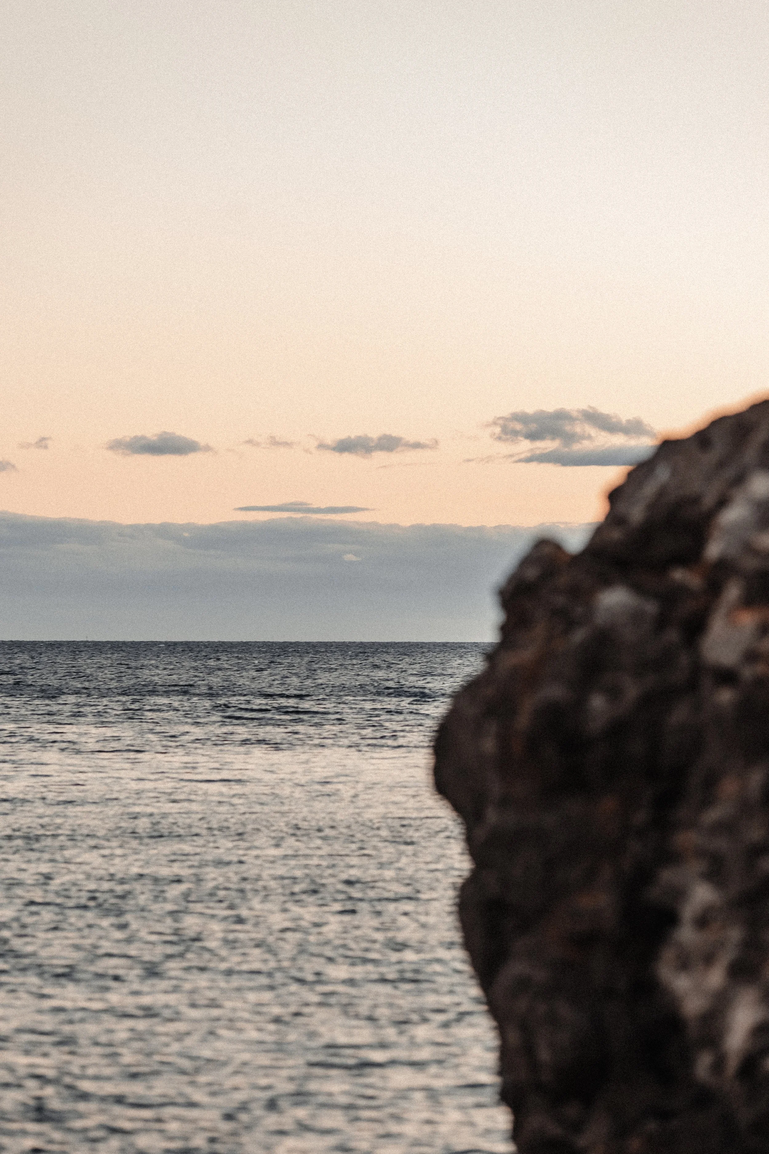 Vue de la mer avec un rocher en premier plan et un ciel au coucher du soleil avec quelques nuages.
