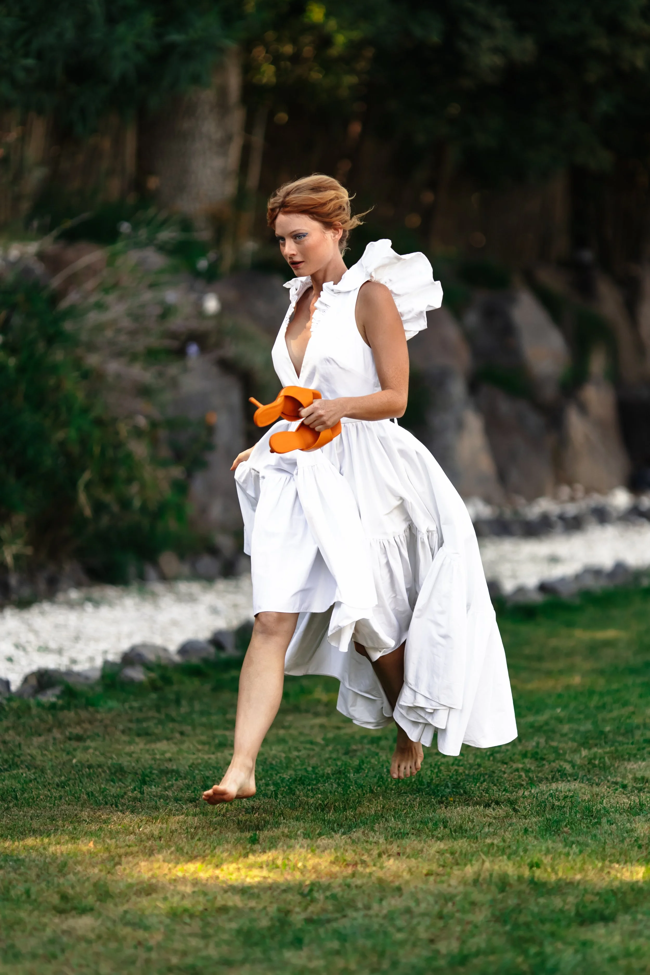 Une femme avec une robe blanche se promène pieds nus dans un jardin.
