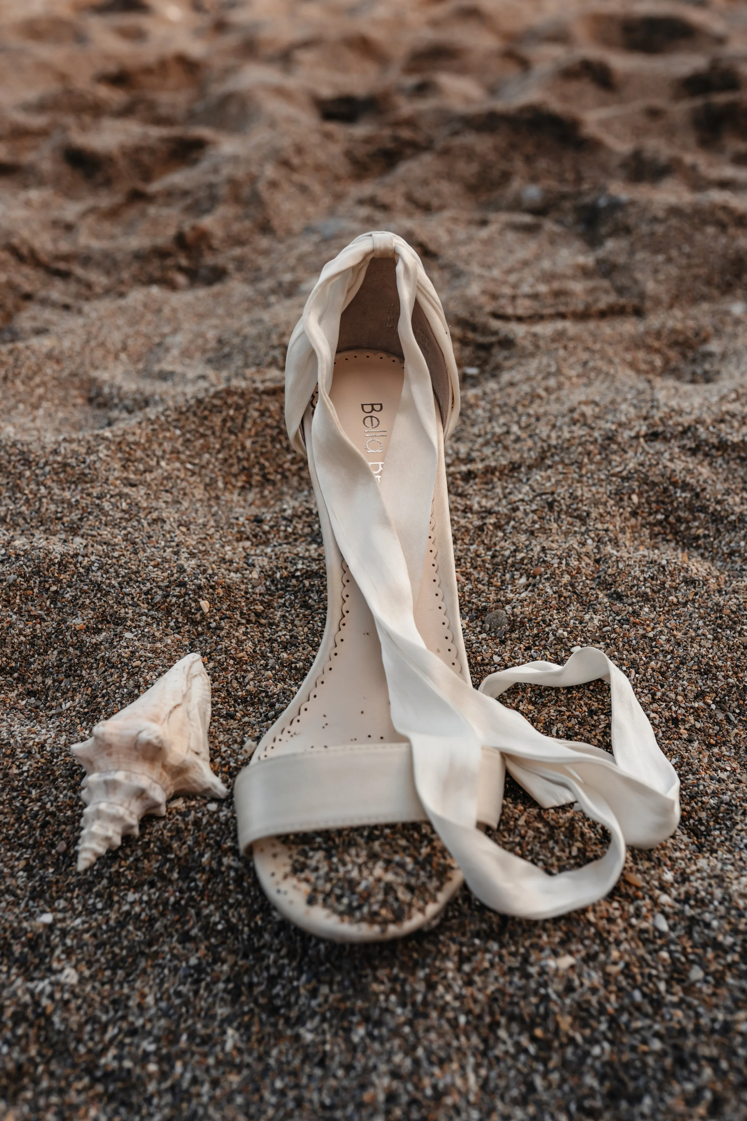 Chaussure de danse blanche abandonnée sur la plage, avec un coquillage à côté.