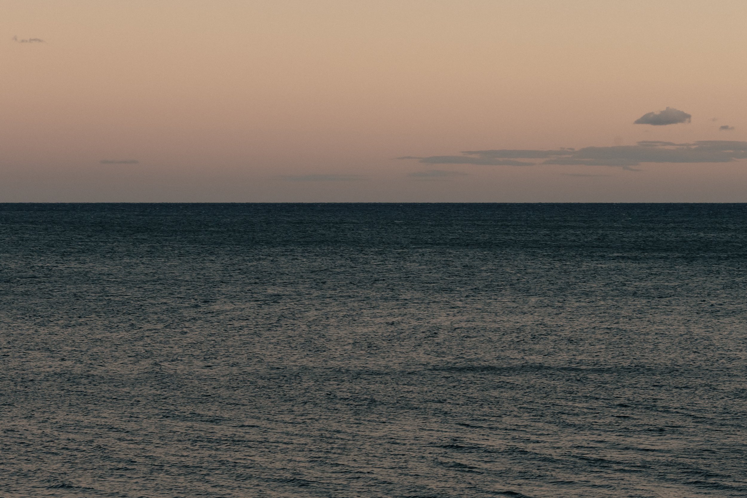 Une mer calme avec un ciel au crépuscule et quelques nuages