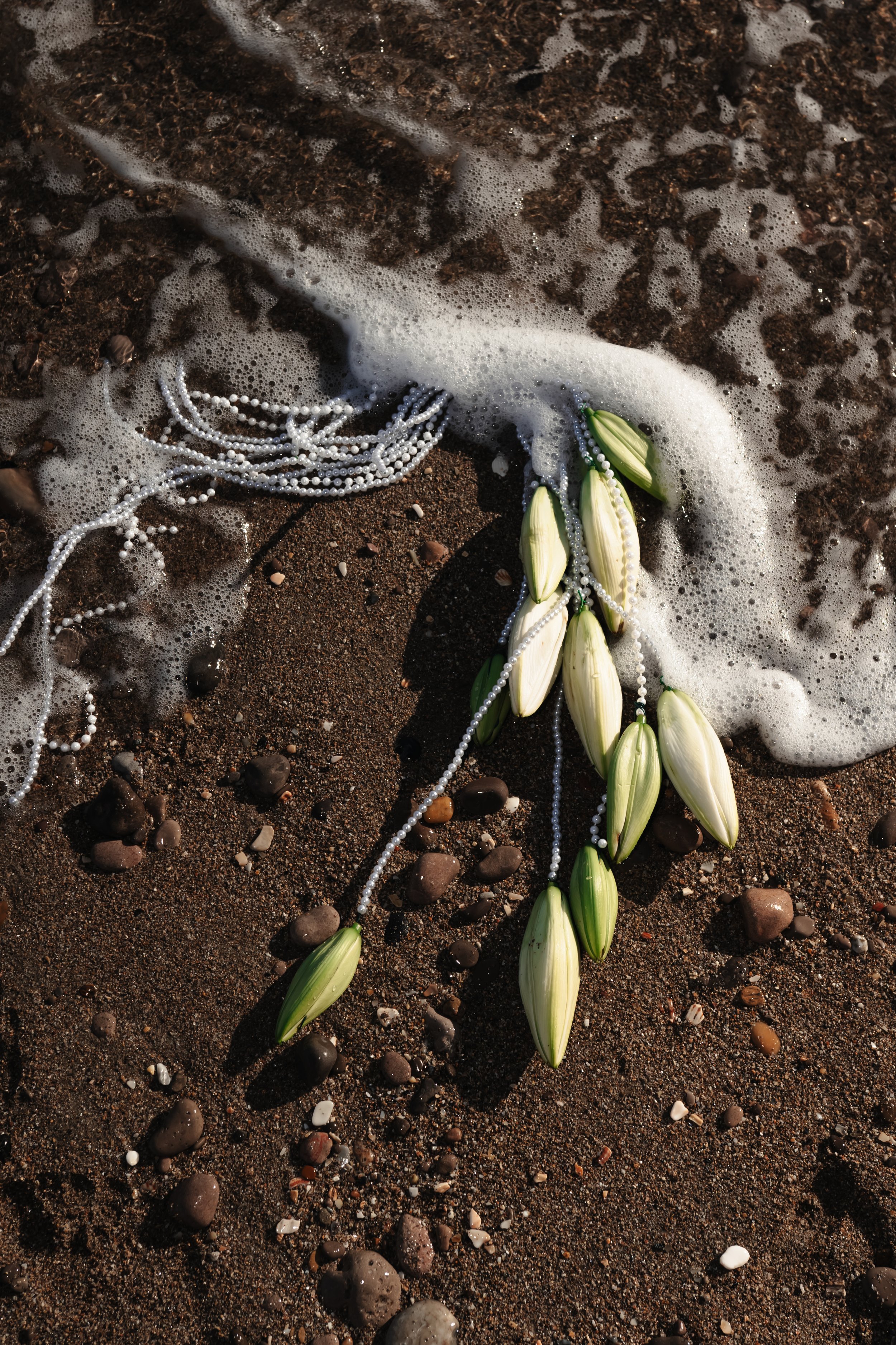 Fleurs blanches avec des perles de décoration sur une plage de sable, partiellement recouvertes par de l'eau de mer avec des bulles.