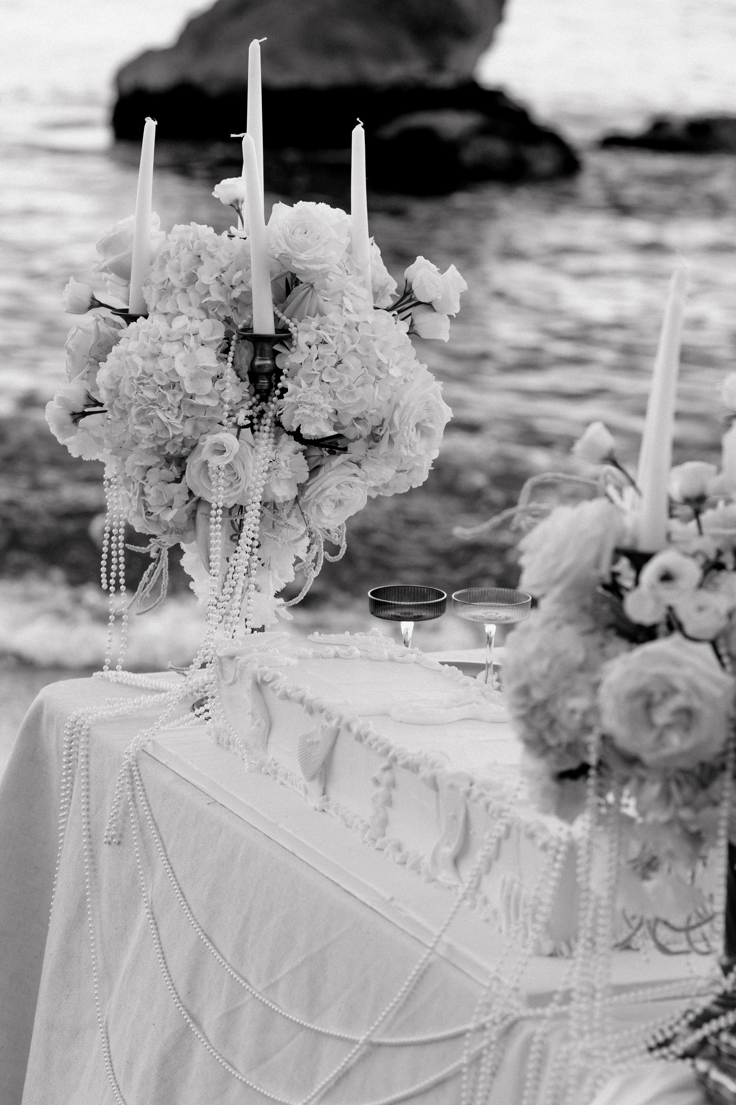 Table de mariage ornée de fleurs, bougies et perles, près de la mer.