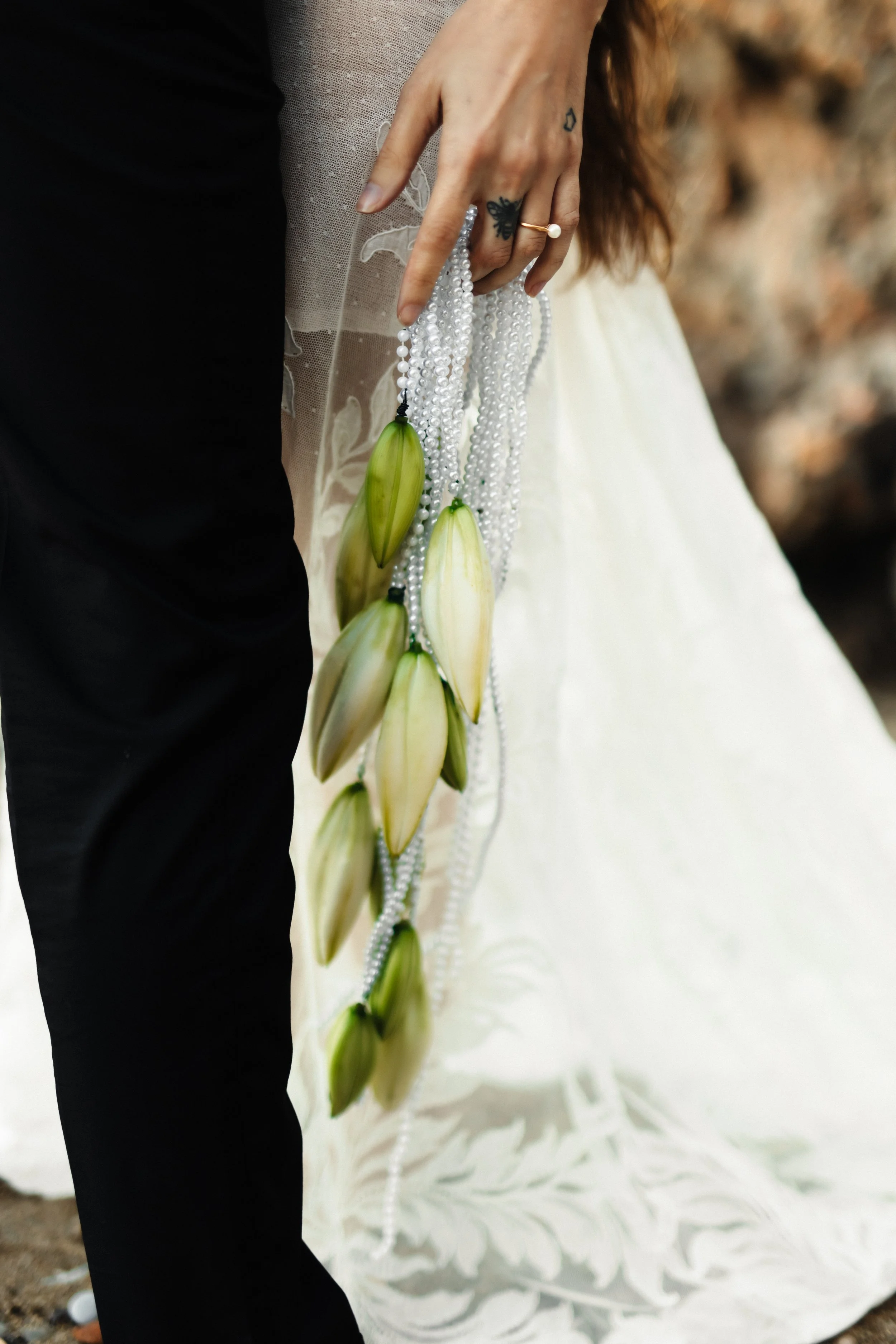 Manche de robe de mariage blanche avec fleurs en strass, personne tenant un collier de perles avec des fleurs en forme de feuilles, fond flou.